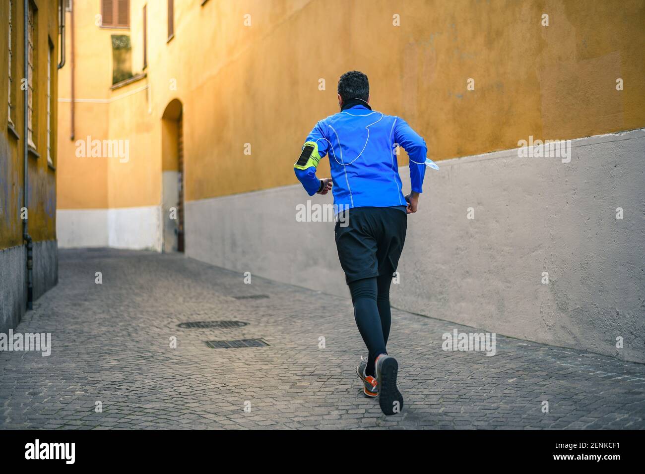 Corsa maschile e musica d'ascolto durante l'allenamento. L'uomo corre in città e fa jogging da solo. Runner con telefono cellulare collegato a una registrazione Smart Watch Foto Stock