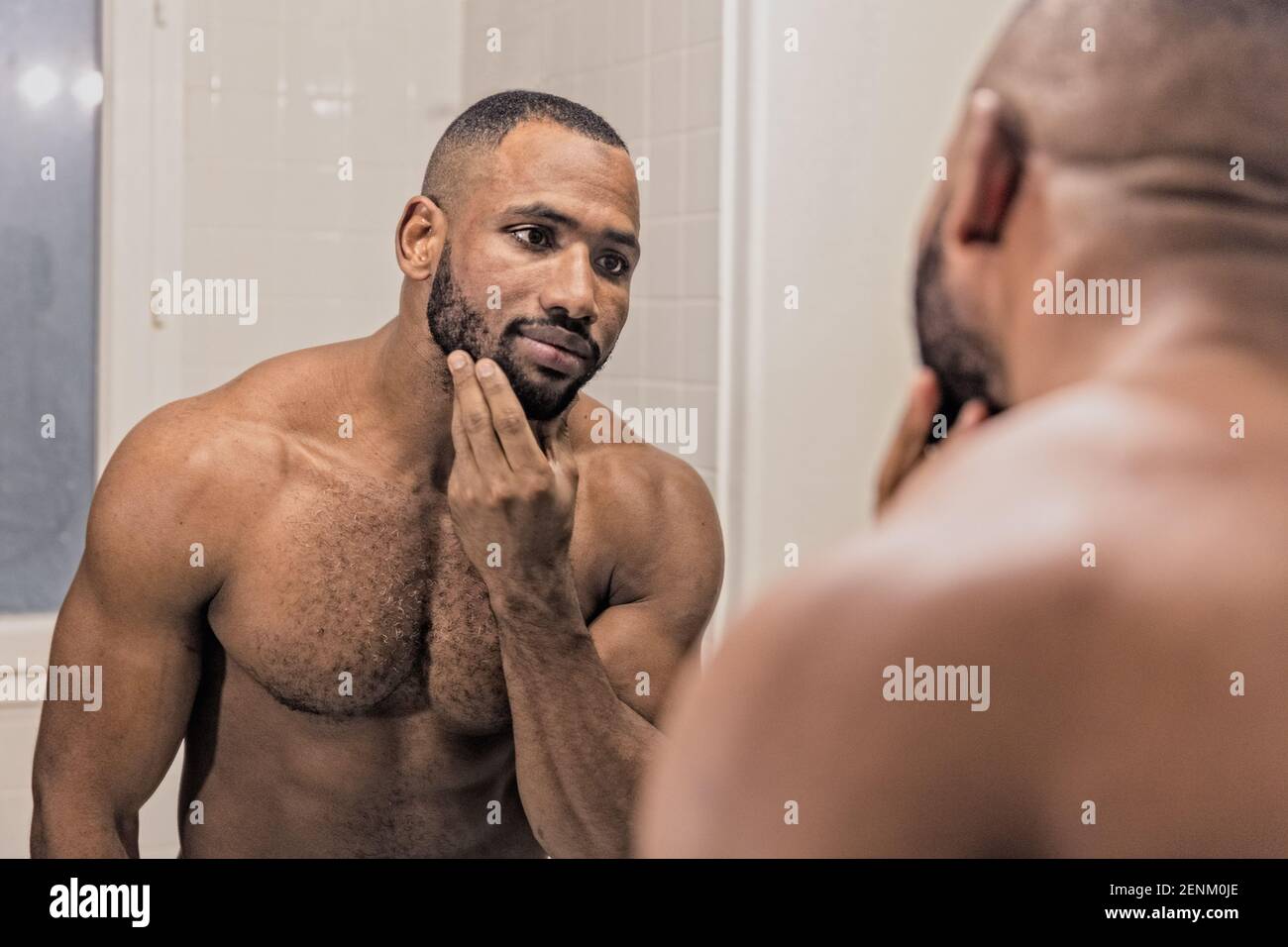 Uomo che guarda nello specchio, tocca la barba Foto Stock