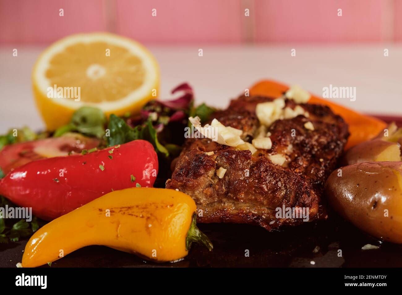 Le costolette di maiale alla griglia sono servite con insalata, limone, peperoni dolci e un bicchiere di vino rosso da gustare con il pasto. Foto Stock