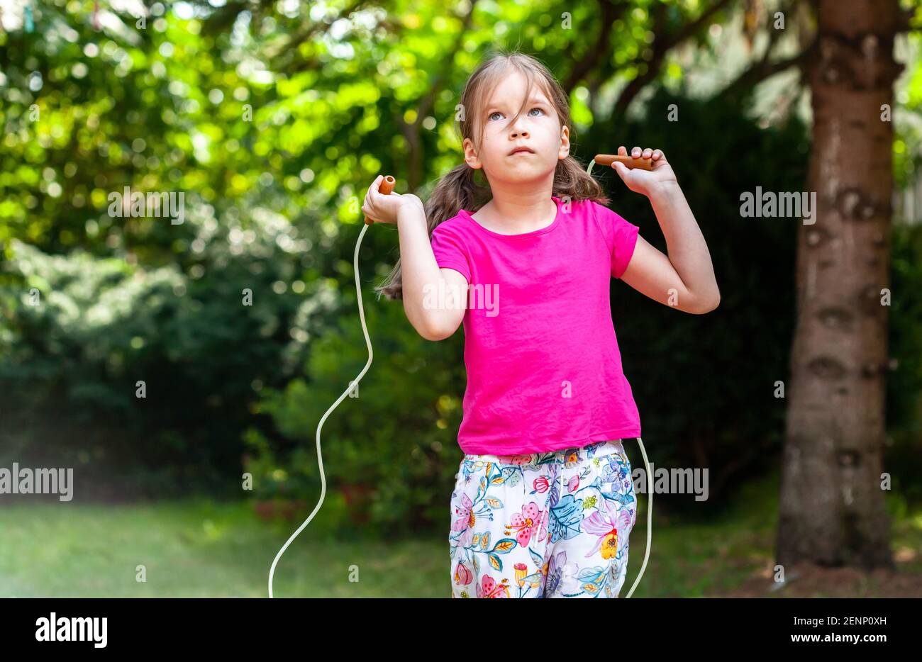 Bambino, una ragazza piccola che salta usando una corda saltante da solo,  tirata di stile di vita all'aperto. Capretto usando una corda di salto  fuori. Bambini in età scolare e a fisica