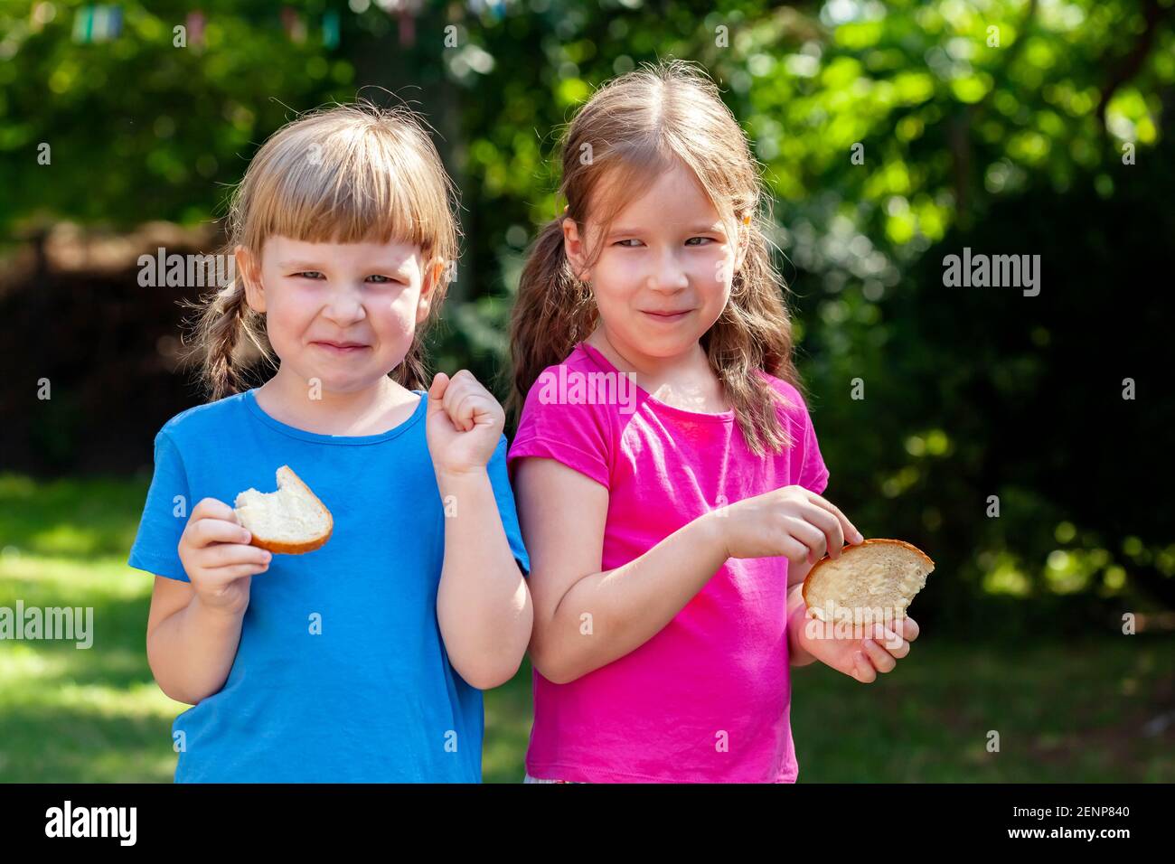 Due ragazze felici mangiano fette di pane con il burro sorridente, ritratto all'aperto. Bambini, sorelle, bambini che mangiano cibo fuori, stile di vita shot, sole Foto Stock
