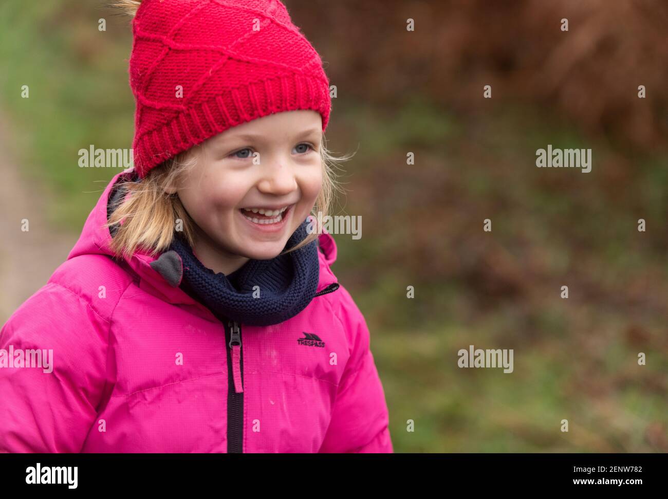 Giovane ragazza in camice rosa invernale e cappello rosso camminando nella foresta, ridendo, sfondo verde, passeggiata invernale nei boschi, lachendes Mädchen im Wald Foto Stock