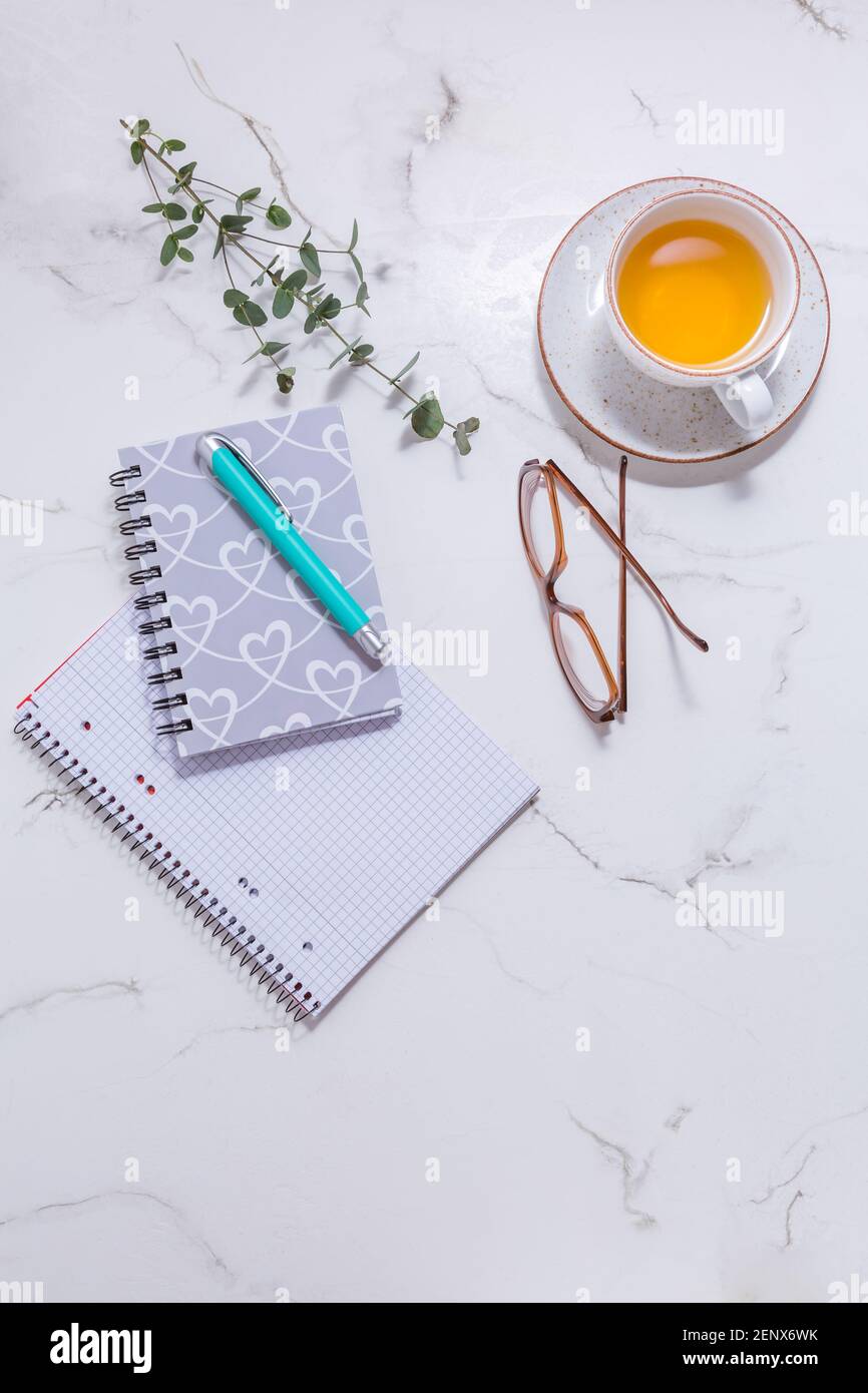 Scrivania da lavoro a casa a disposizione piatta - tazza di tè, con dispositivo di comunicazione e strumenti di scrittura. Business mockup femminile, copyspace, sfondo bianco. Foto Stock