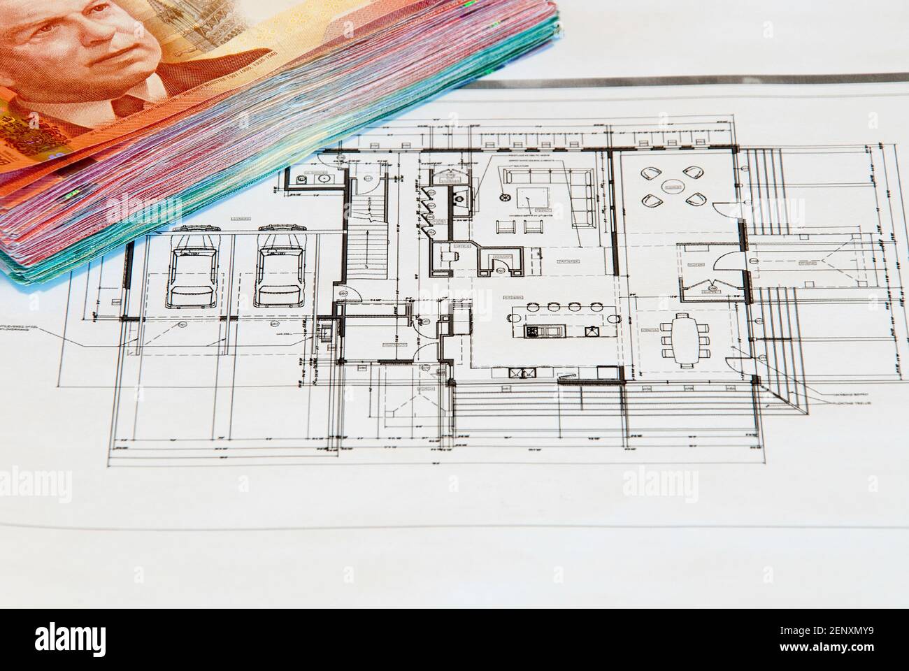 Finanziamento di un progetto di costruzione. Disegno della casa su carta bianca con un mucchio di soldi sul bordo Foto Stock