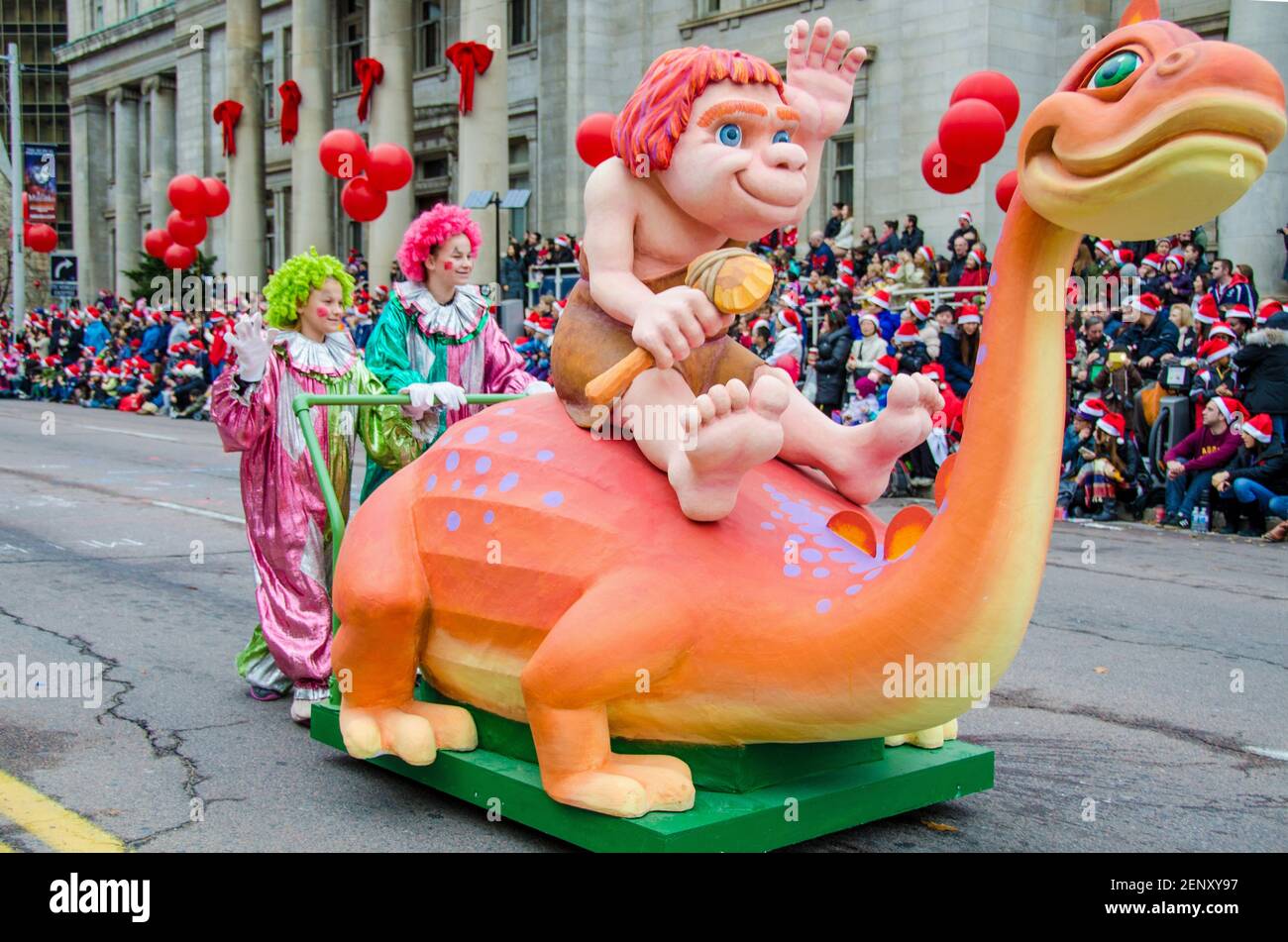 Caveman in sella a un mini galleggiante di dinosauro nella celebrazione della 109a edizione della Parata di Babbo Natale. Più di mezzo milione di persone partecipano al par Foto Stock