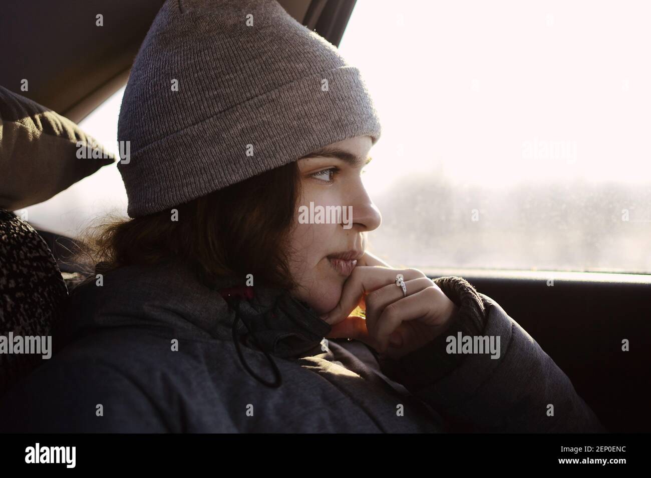 Una ragazza in abiti grigi guarda fuori il finestrino dell'auto, si appoggia sulla sua mano. Foto Stock