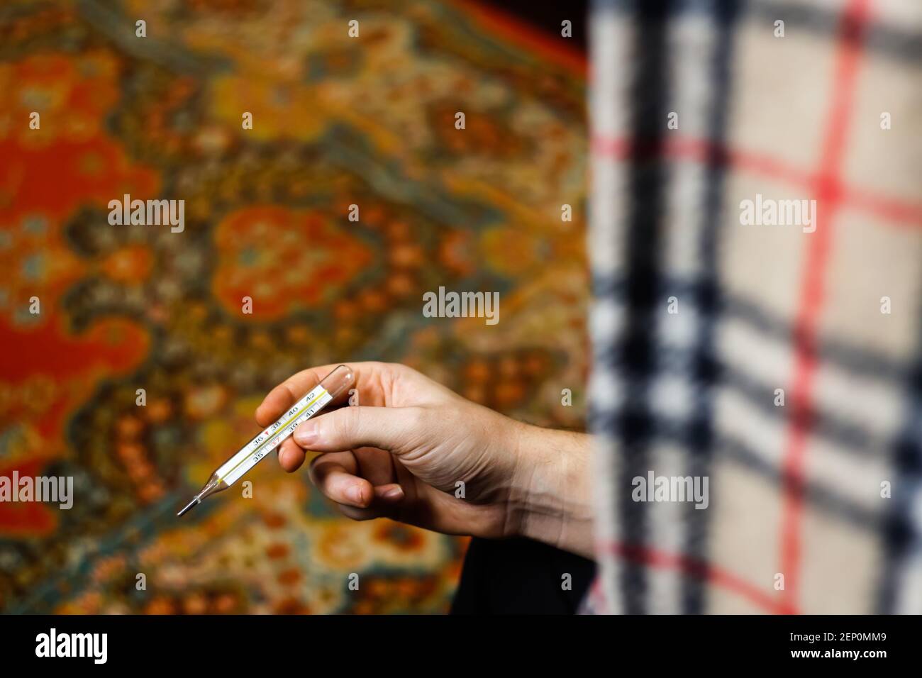 Mani che tengono un termometro. L'uomo controlla la temperatura del corpo, il giovane malato con una temperatura, uno sguardo sulla spalla. Messa a fuoco selettiva Foto Stock