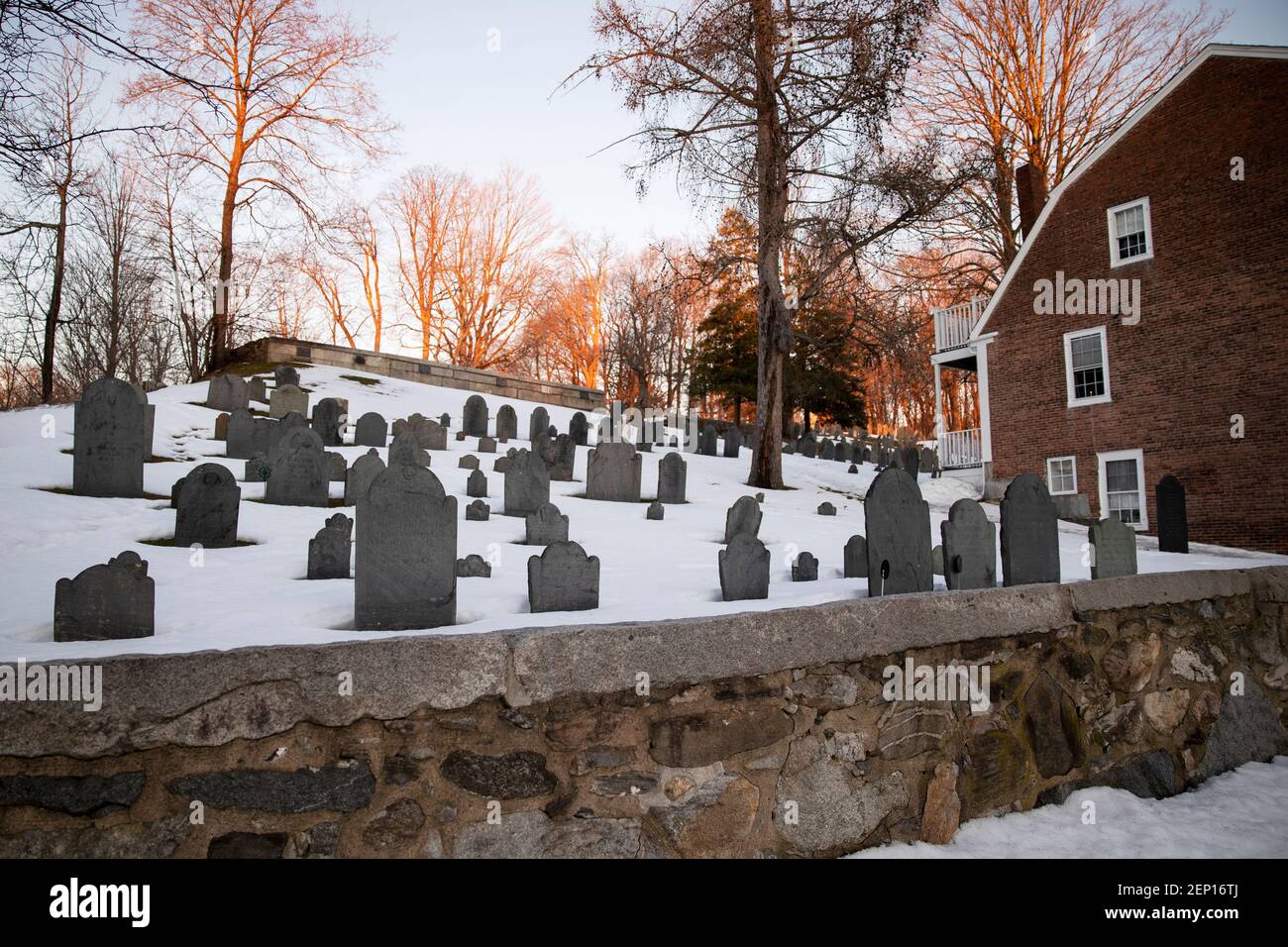 Gli alberi invernali si illuminano al tramonto presso il terreno di sepoltura di Old Hill su Monument Square, il cimitero più antico della storica Concord, Massachusetts, USA. Foto Stock