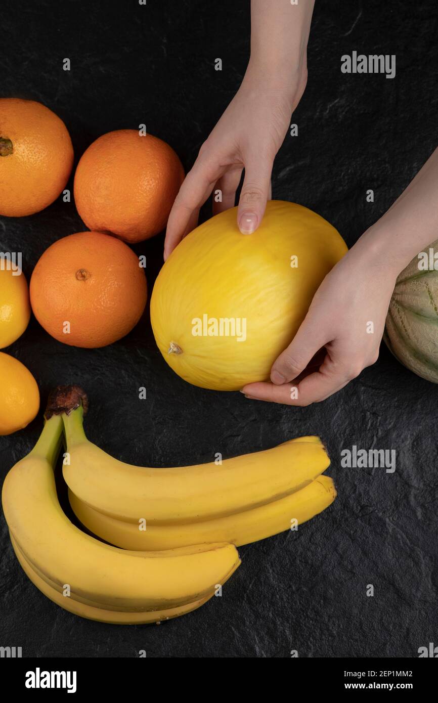 Mani femminili che tengono il melone maturo sul tavolo nero Foto Stock