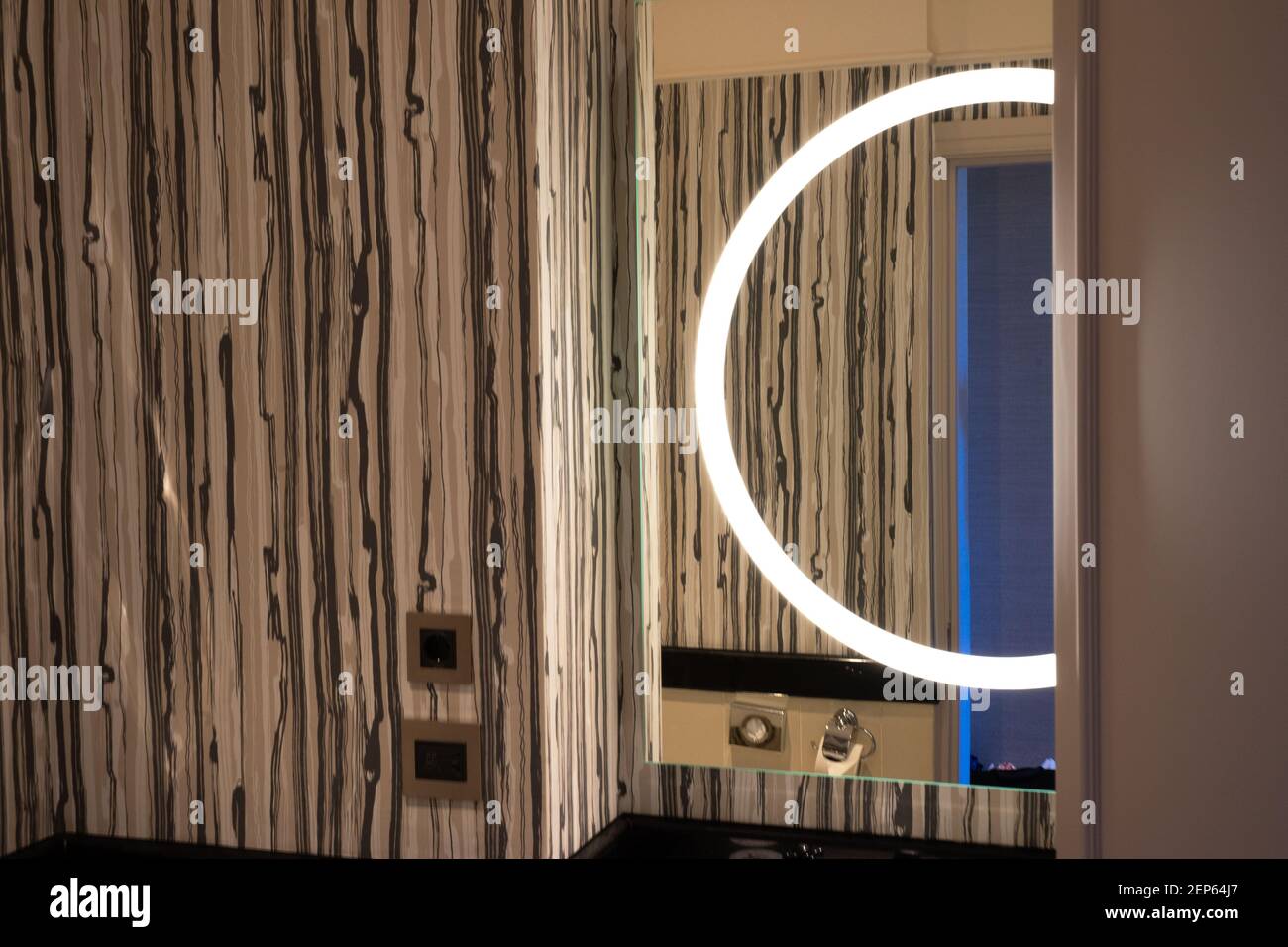 Decorazione moderna del bagno, che include lo spazio sopra il lavandino, lampada rotonda riflessa nello specchio, motivo ornamentale marrone su una parete Foto Stock