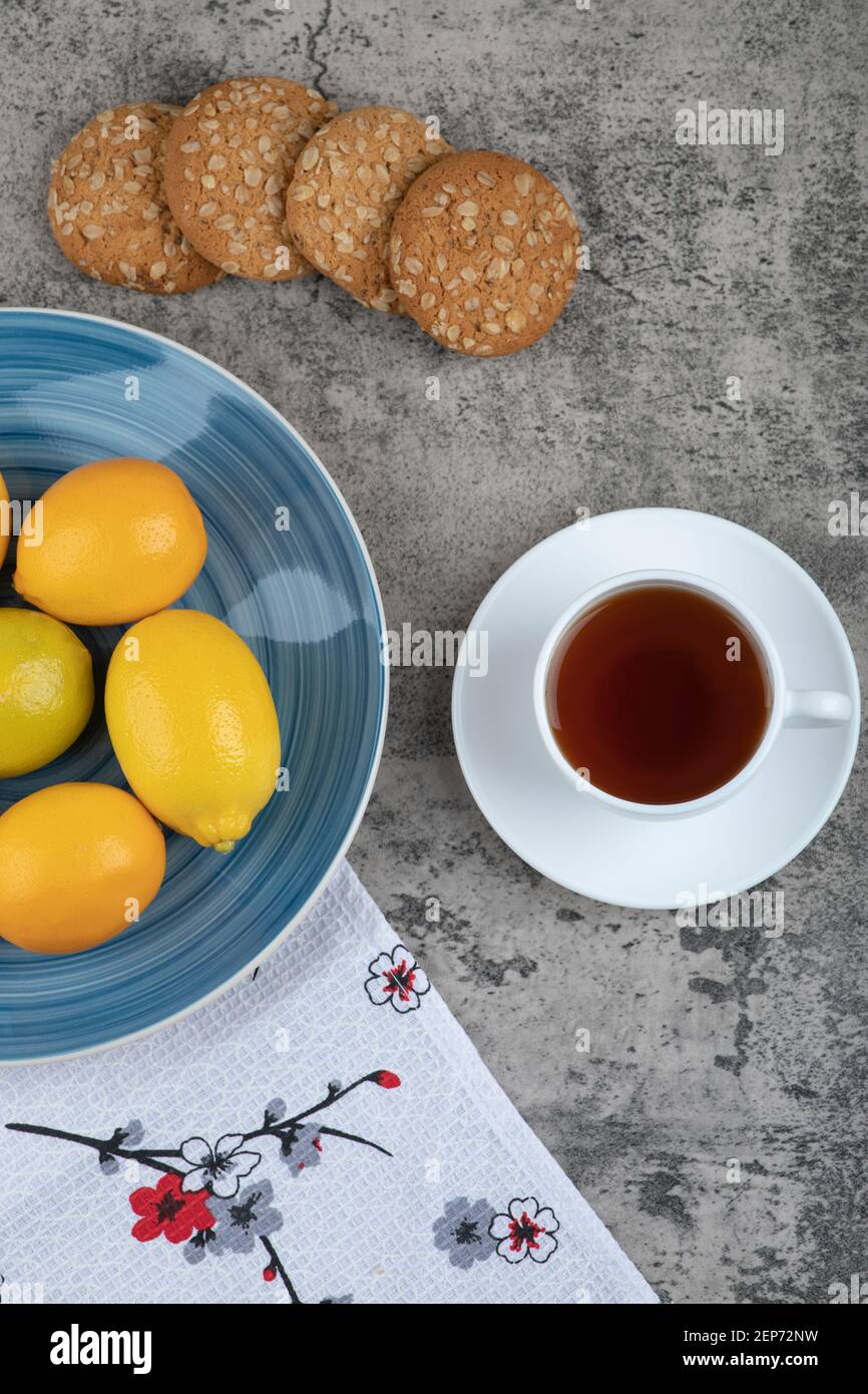 Tazza di tè caldo, piatto di limoni e deliziosi biscotti sulla superficie di pietra Foto Stock