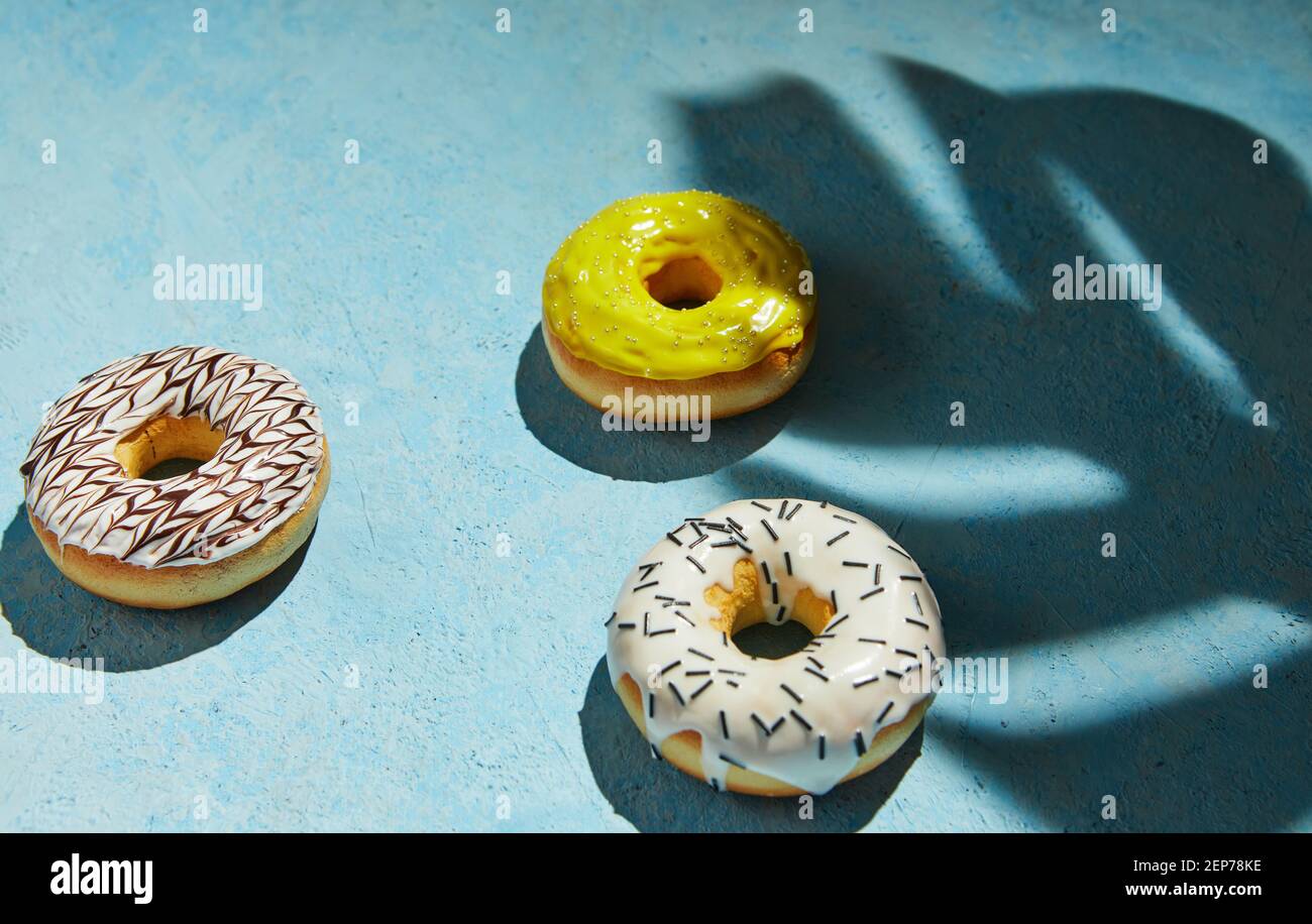 Ciambelle multicolori con glassatura, spruzzi con ombra da foglia di monstera su sfondo blu. Foto Stock