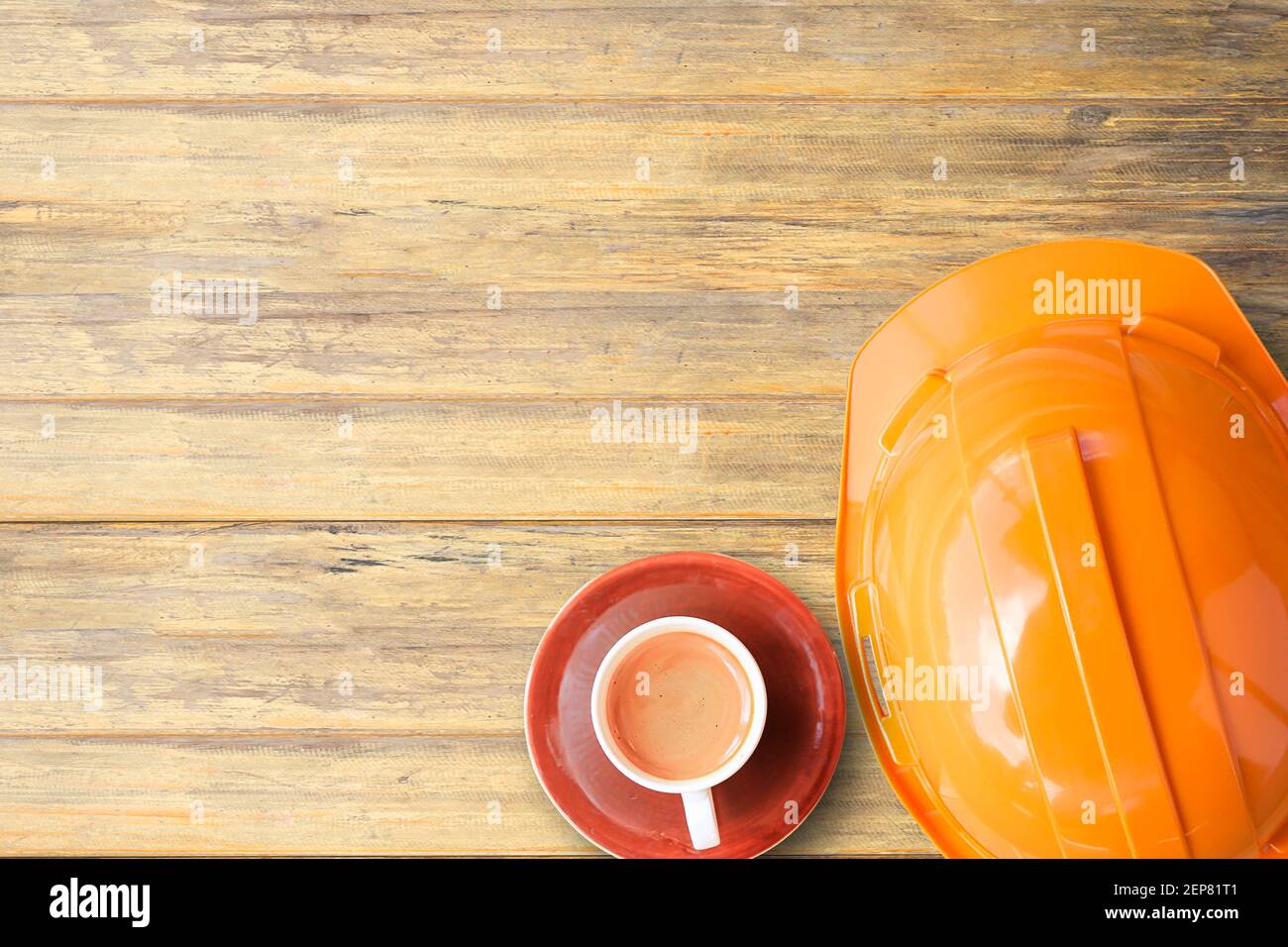 Casco e tazza di caffè Orange Safety Engineer su sfondo tavola in legno. Elmetto di sicurezza industriale protezione del lavoro e prevenzione degli incidenti. Vista dall'alto Foto Stock