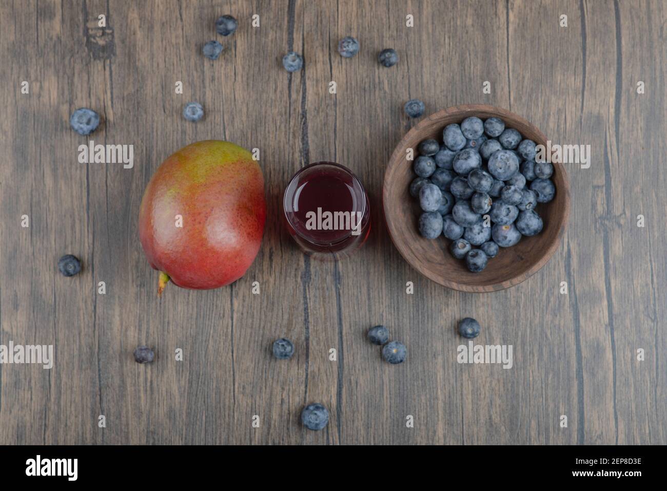 Mango intero, mirtilli e bicchiere di succo fresco su tavolo di legno Foto Stock