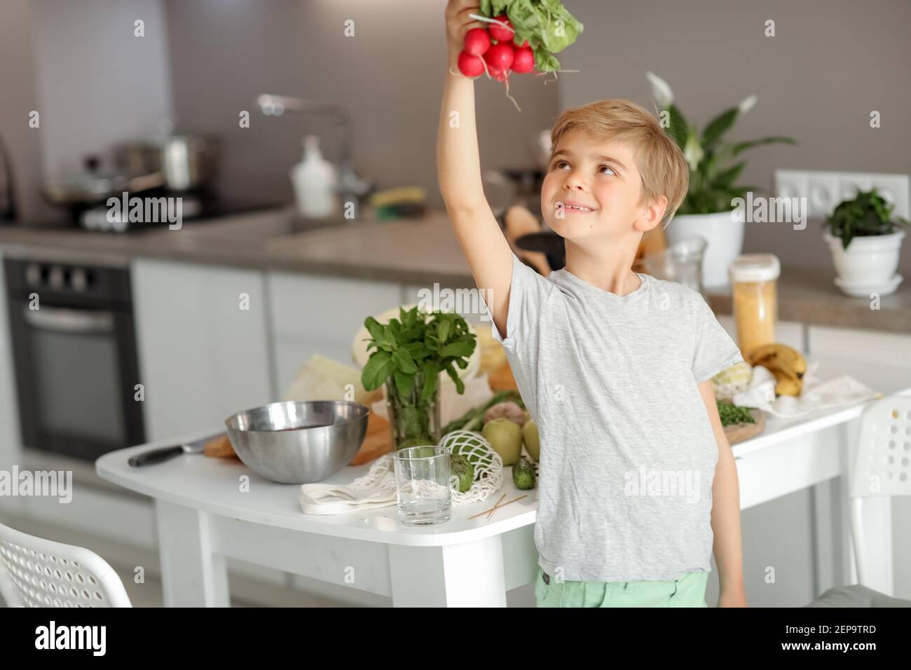 Il bambino mette le verdure sul tavolo e prepara un'insalata. Foto Stock