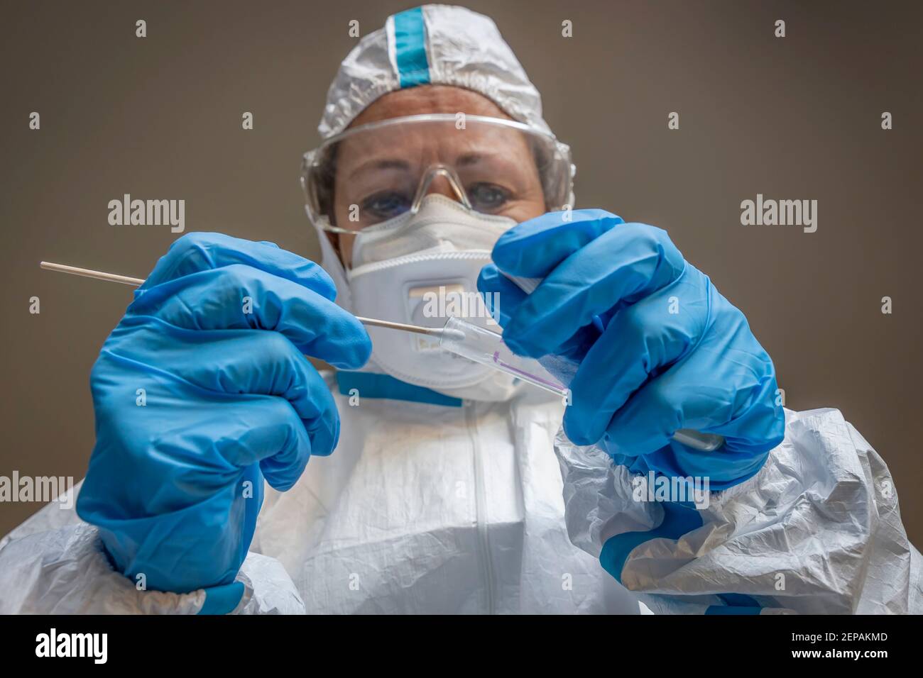 Una donna, tecnico di laboratorio, completamente coperta in una tuta protettiva bianca, fa un tampone di prova per controllare una possibile infezione con Coronavirus Foto Stock