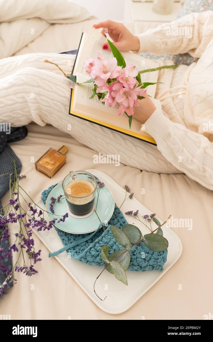 Donna che legge un libro a letto accanto alla sua colazione al caffè. Lei  sta tenendo un bel bouquet di fiori con la sua mano sinistra Foto stock -  Alamy