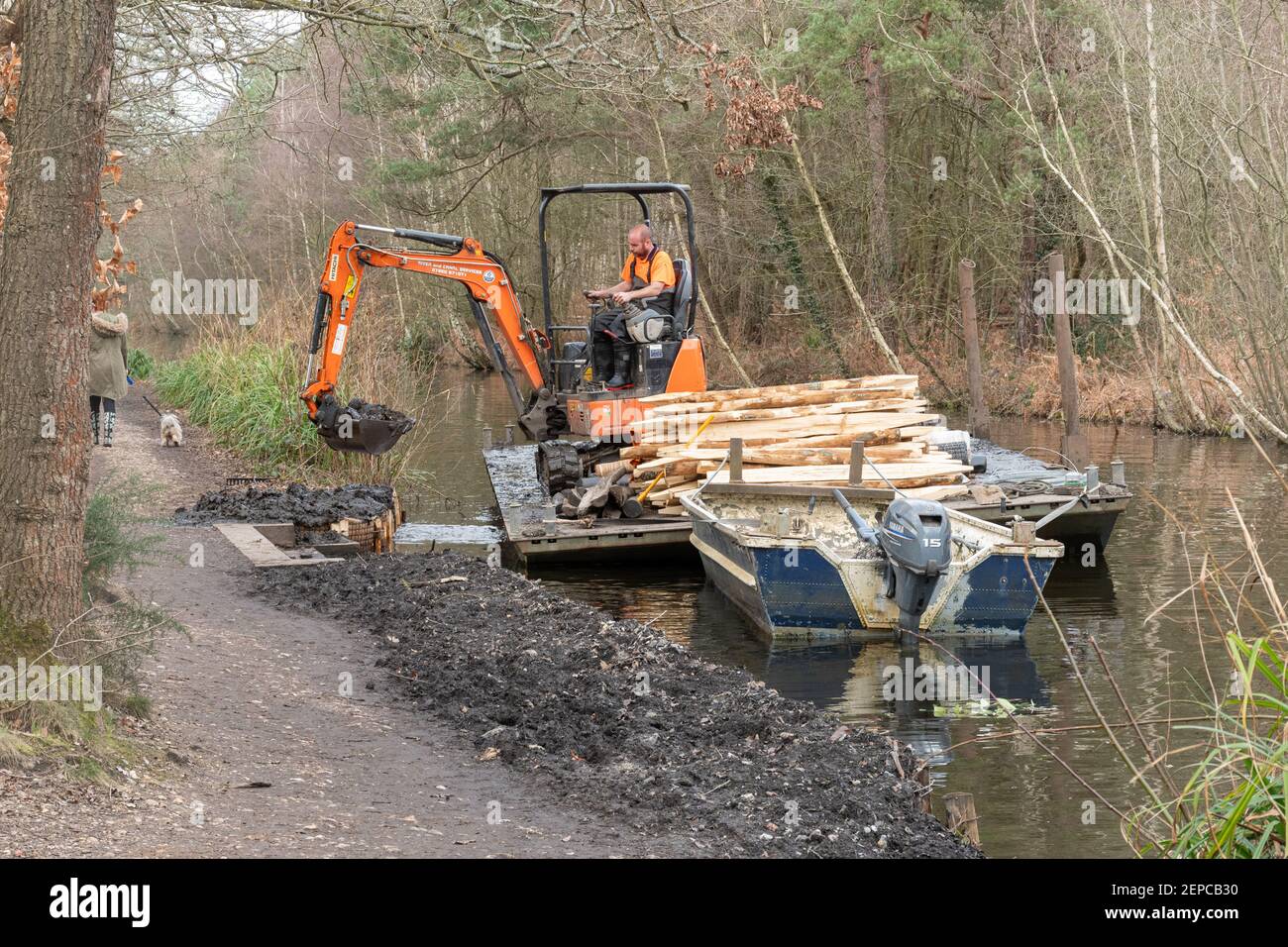Uomo che lavora in un escavatore o digger su un pontile di lavoro galleggiante che ripara una banca di canale erosa sul canale di Basingstoke in Surrey, Regno Unito Foto Stock
