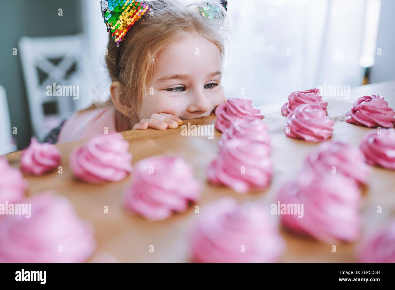 Bambina con i capelli biondi e gli occhi blu guardare su deliziosi marshmallow rosa fatto in casa ot zephyr sul tavolo in cucina. Foto Stock