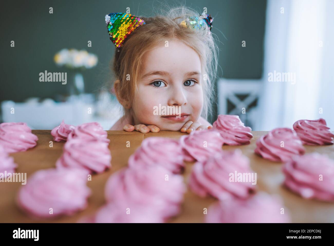 Bambina con i capelli biondi e gli occhi blu guardare su deliziosi marshmallow rosa fatto in casa ot zephyr sul tavolo in cucina. Foto Stock