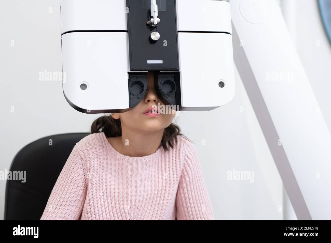 Carino scolaro elementare seduto di fronte a apparecchiatura oftalmologica mentre avere la sua vista controllata in cliniche contemporanee Foto Stock