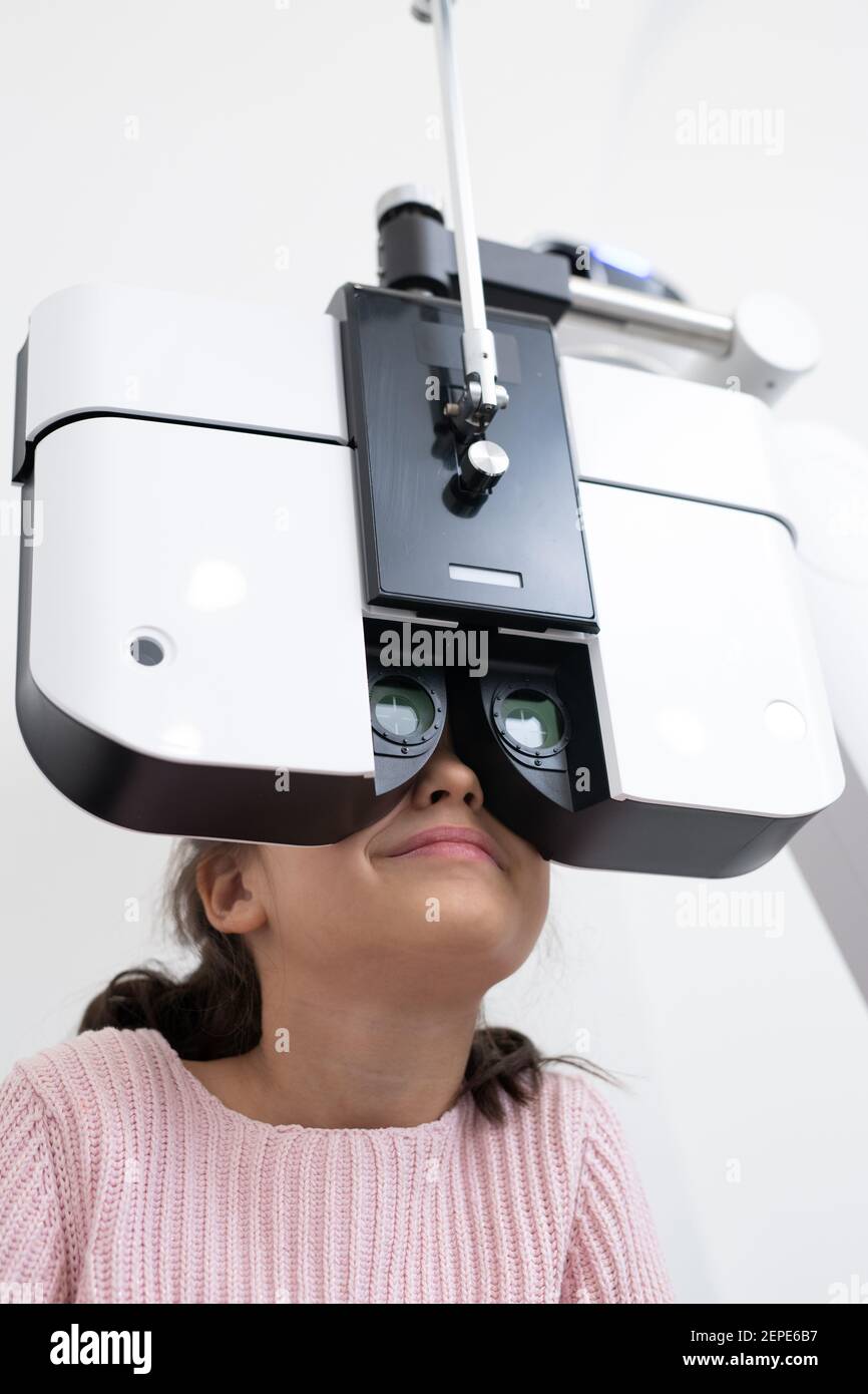 Scolaro elementare seduto di fronte ad apparecchiature oftalmologiche mentre ha la sua vista si è verificata in cliniche contemporanee Foto Stock