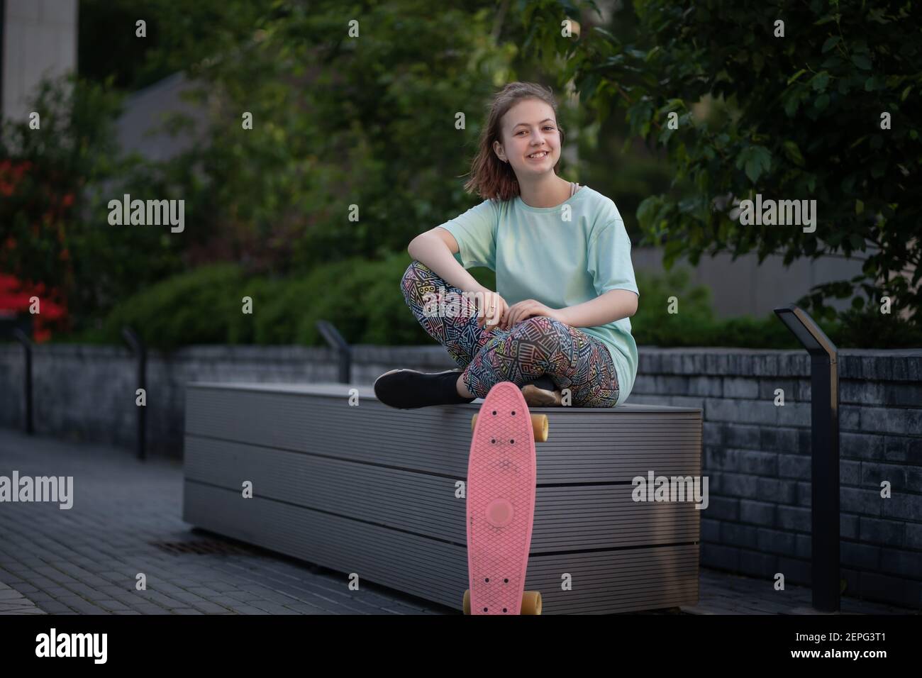 elegante adolescente sedersi e riposarsi con penny board dopo lo skateboard in strada Foto Stock