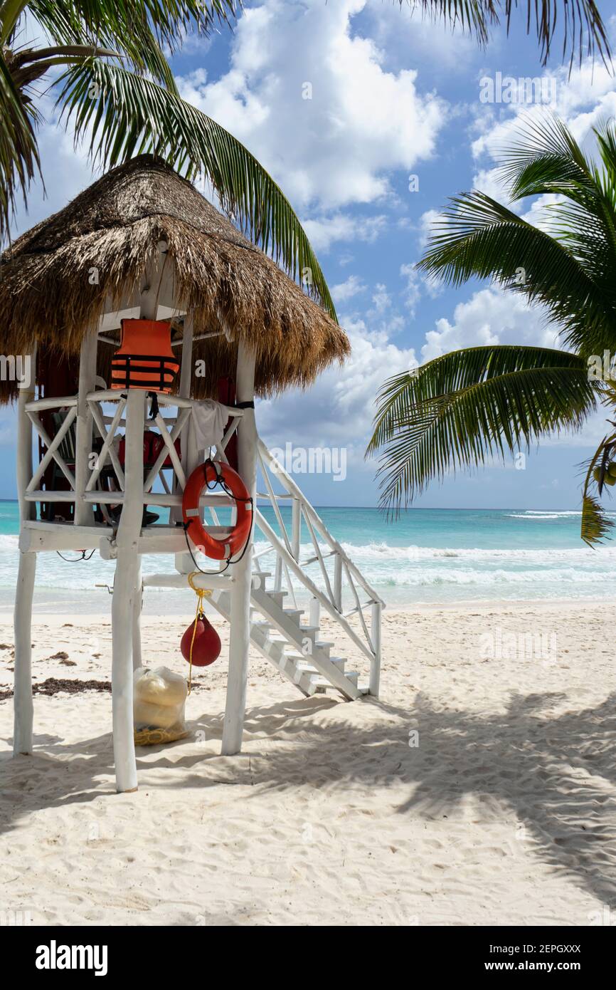 Torre del bagnino sulla spiaggia dei Caraibi, con sabbia piatta, palme intorno, e il mare turchese. Sullo sfondo il cielo nuvoloso e l'Oceano Foto Stock