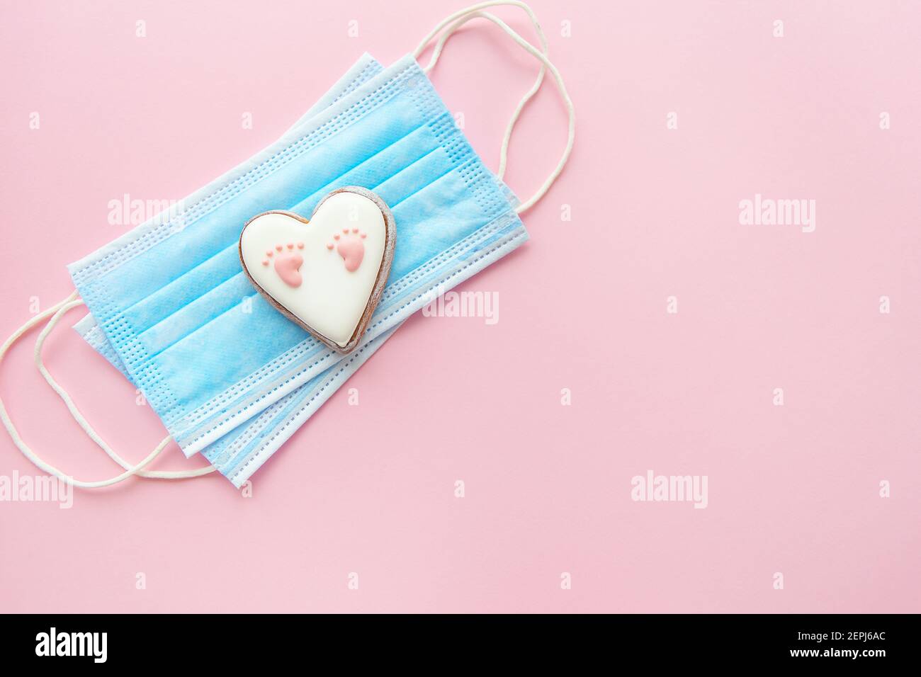 Maschera medica monouso e cuore con impronta del bambino su sfondo rosa. Parto durante la pandemia del coronavirus Foto Stock