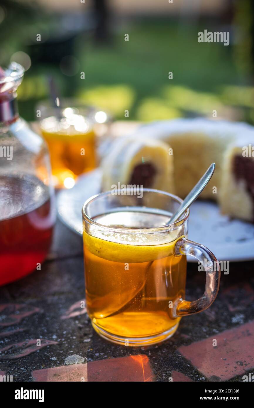 Rinfresco con tè e torta in giardino. Colazione all'aperto. Bicchiere di tè alle erbe con limone e cucchiaio sul tavolo Foto Stock
