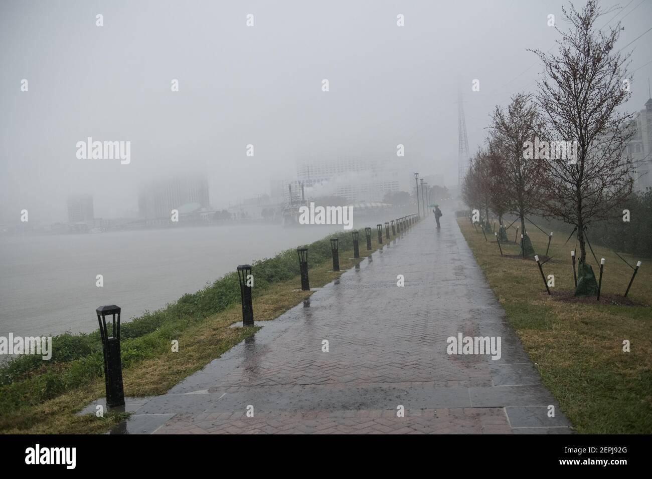 Figure sagomate con ombrelli camminano lungo il nebbioso lungofiume del Mississippi, passando davanti allo storico battello a vapore Natchez a New Orleans. Foto Stock