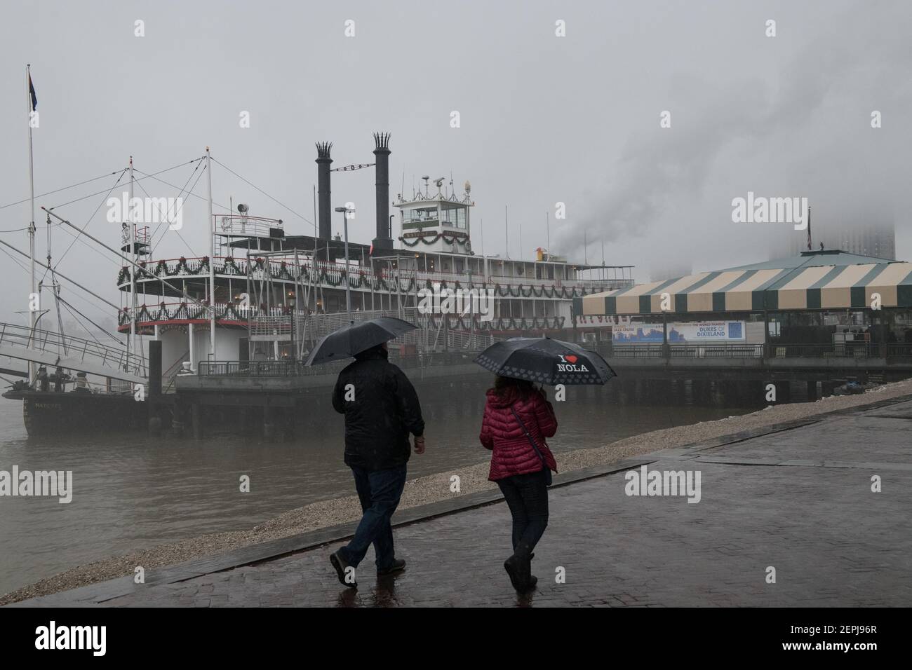 Figure sagomate con ombrelli camminano lungo il nebbioso lungofiume del Mississippi, passando davanti allo storico battello a vapore Natchez a New Orleans. Foto Stock