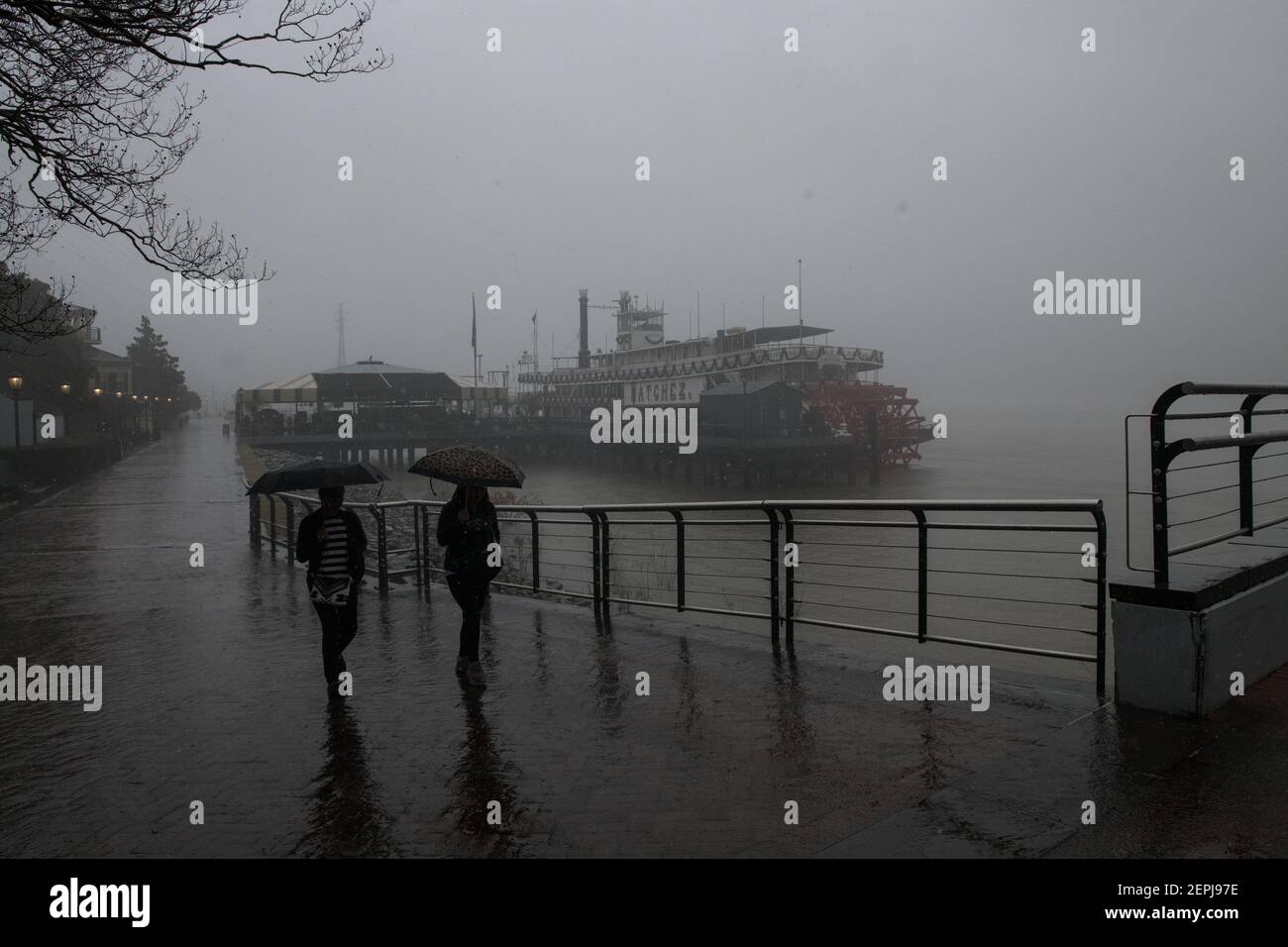 Figure sagomate con ombrelli camminano lungo il nebbioso lungofiume del Mississippi, passando davanti allo storico battello a vapore Natchez a New Orleans. Foto Stock