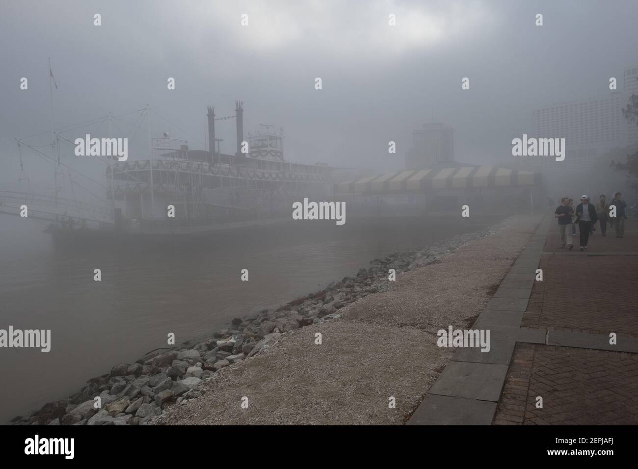 Figure sagomate con ombrelli camminano lungo il nebbioso lungofiume del Mississippi, passando davanti allo storico battello a vapore Natchez a New Orleans. Foto Stock