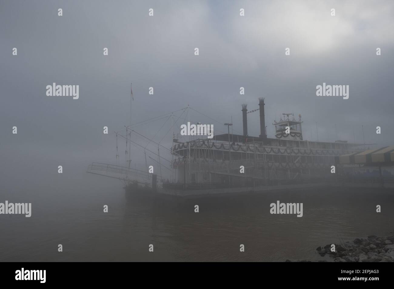 Figure sagomate con ombrelli camminano lungo il nebbioso lungofiume del Mississippi, passando davanti allo storico battello a vapore Natchez a New Orleans. Foto Stock