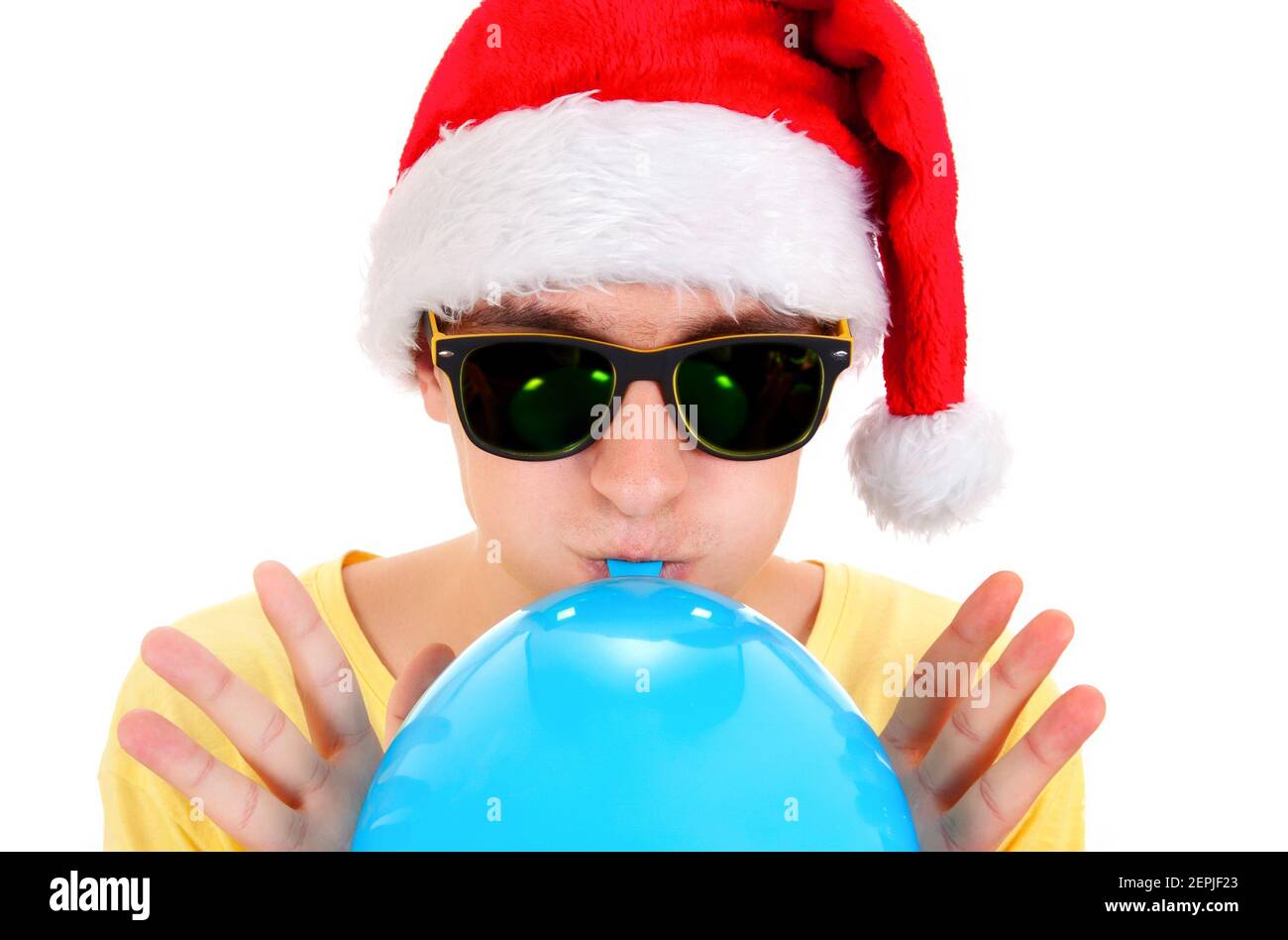 Young Man in Santa Hat e occhiali da sole gonfiano un Blu Palloncino sul primo piano di sfondo bianco Foto Stock