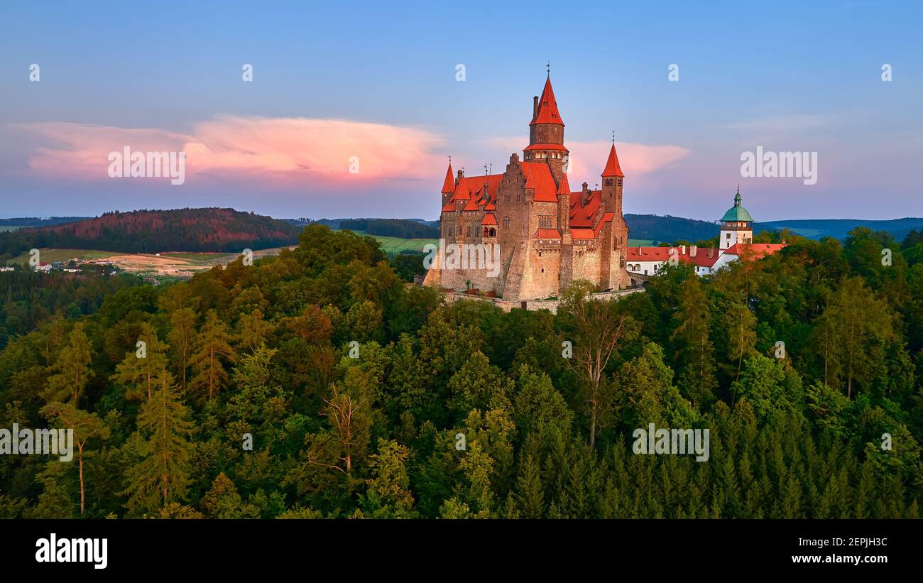 Vista aerea su un romantico castello da favola con alte torri, tetti rossi, muri in pietra circondati da alberi. Castello di Bouzov, regione della Moravia, Repubblica Ceca. Foto Stock