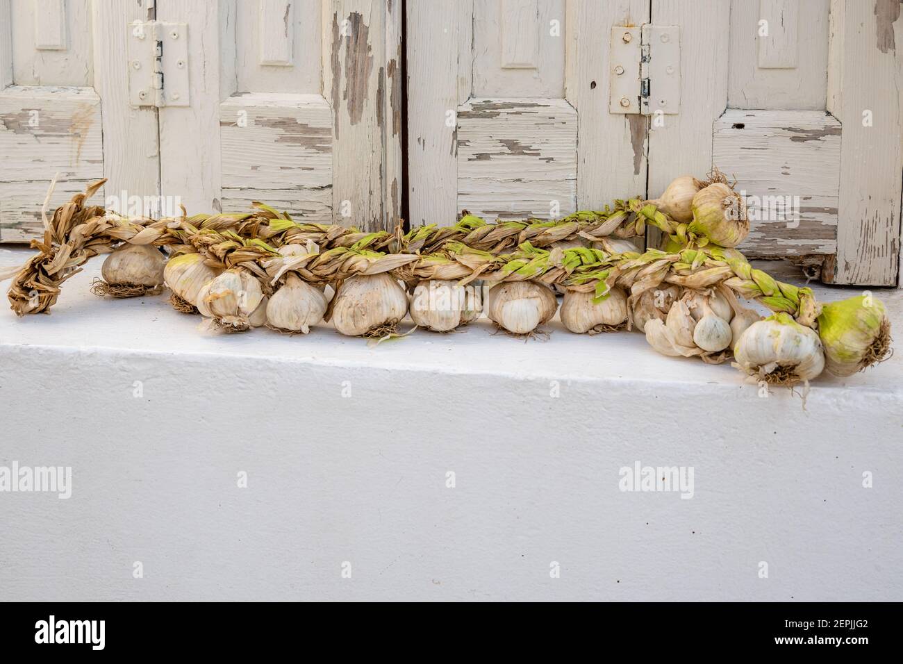 Aglio intrecciato di fronte a persiane bianche, decorazione su strada nella città di Chora sull'isola di Folegandros. CICLADI, Grecia Foto Stock