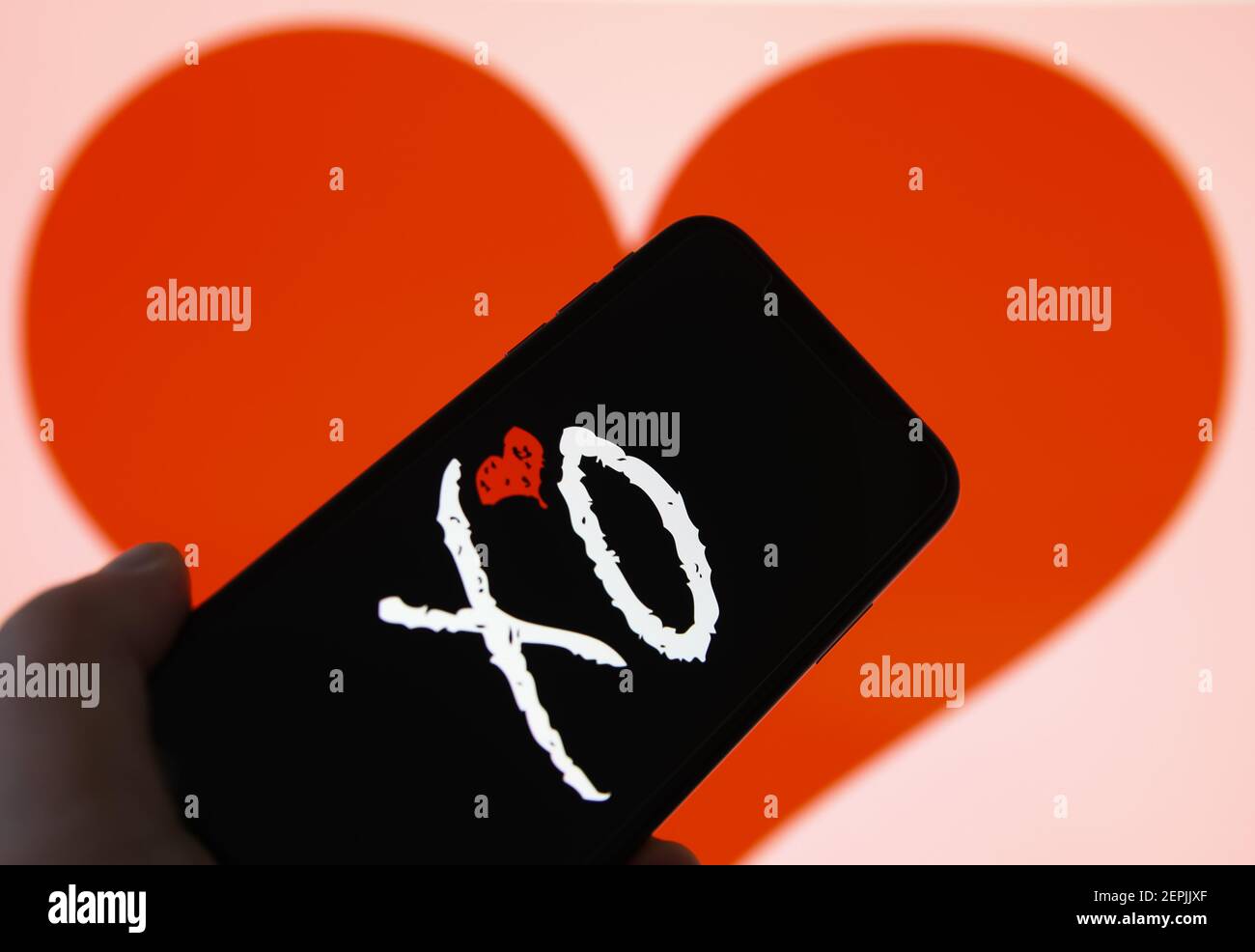 Viersen, Germania - 9 febbraio. 2021: Primo piano dello schermo del telefono cellulare con la scritta del logo dell'app XO dell'agenzia di incontri online, sfondo del cuore sfocato Foto Stock