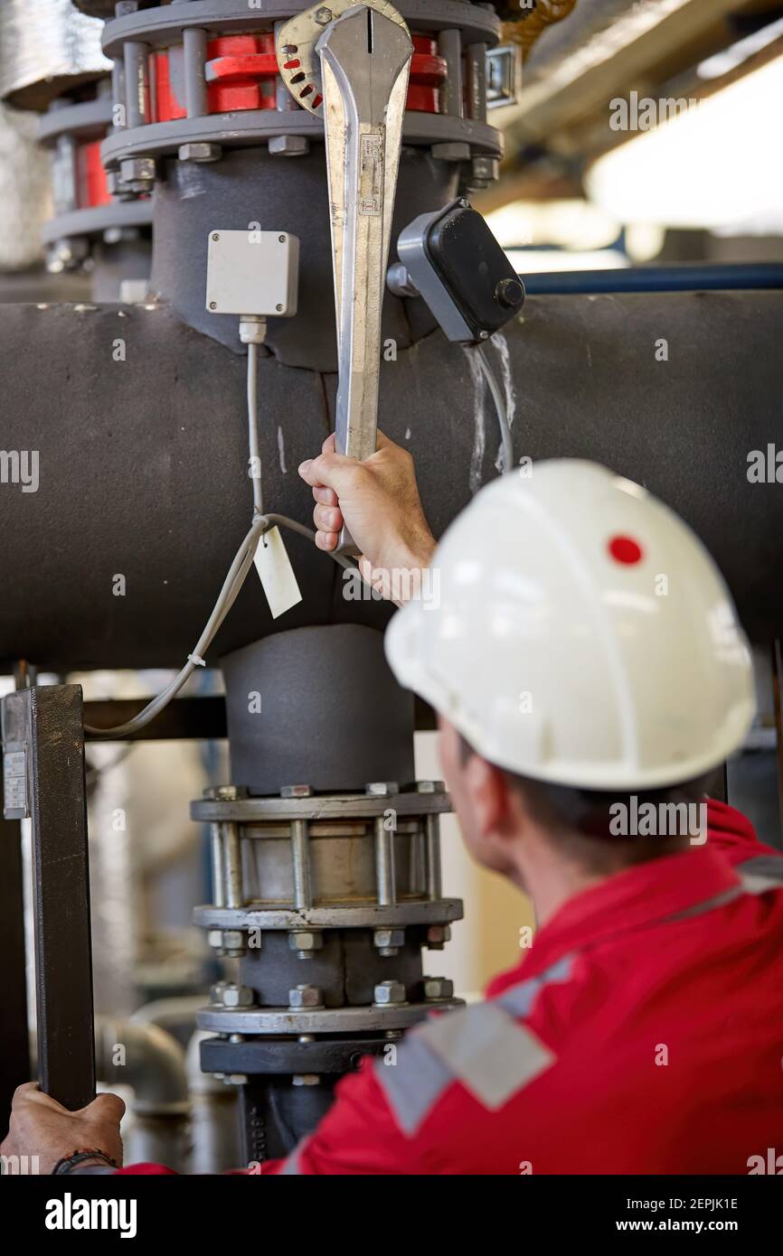Industria energetica. Un tecnico vestito con tute rosse e un casco bianco che controlla i parametri di riscaldamento. Tecnologia di distribuzione dell'acqua di riscaldamento. Foto Stock