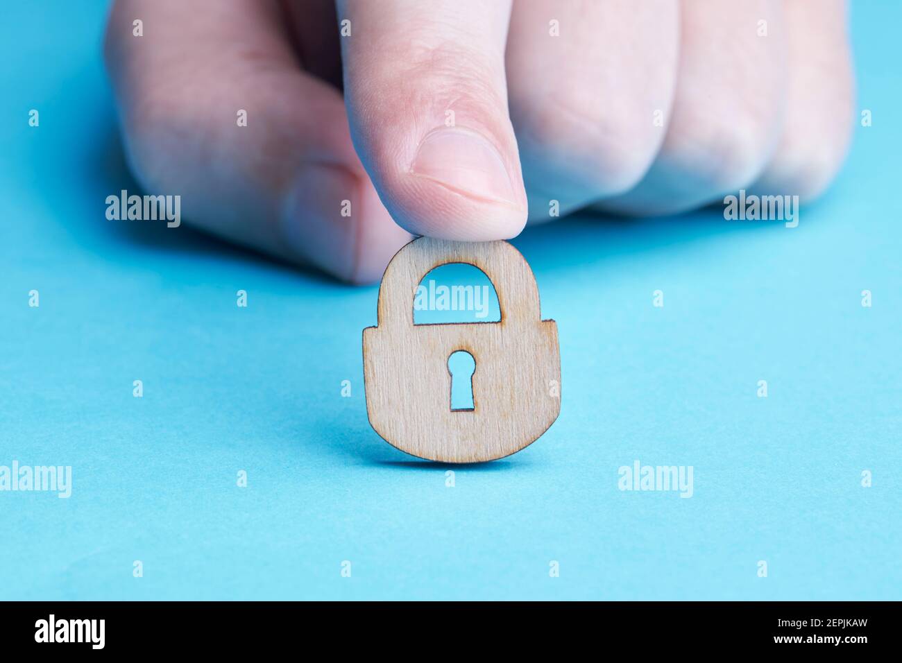 persona privacy e sicurezza concetto. persona caucasica tiene in legno lucchetto su sfondo blu. copia spazio Foto Stock