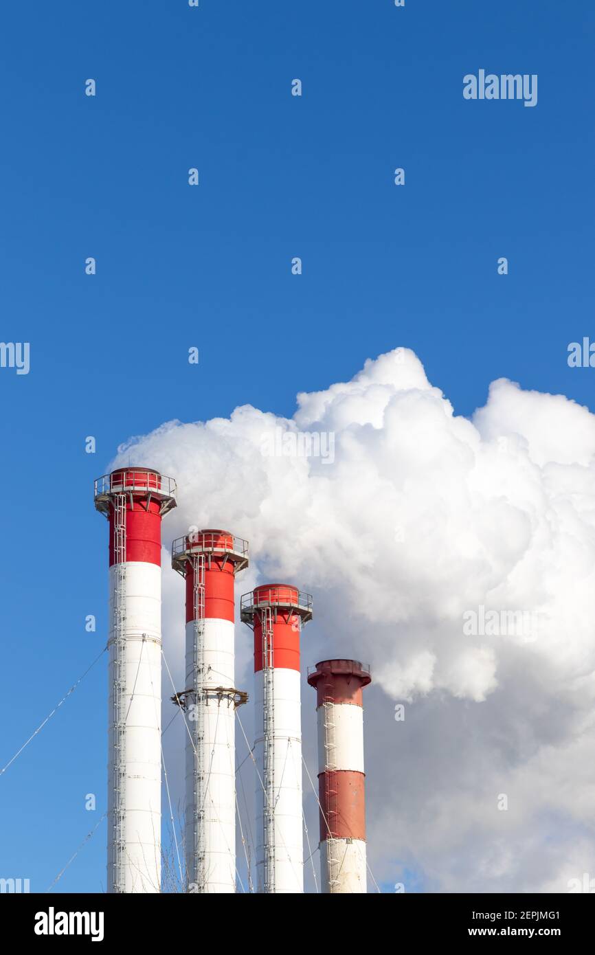 camini rosso-bianco del locale caldaia, dotati di un semaforo. fumo bianco contro il cielo blu nella soleggiata giornata invernale gelida Foto Stock