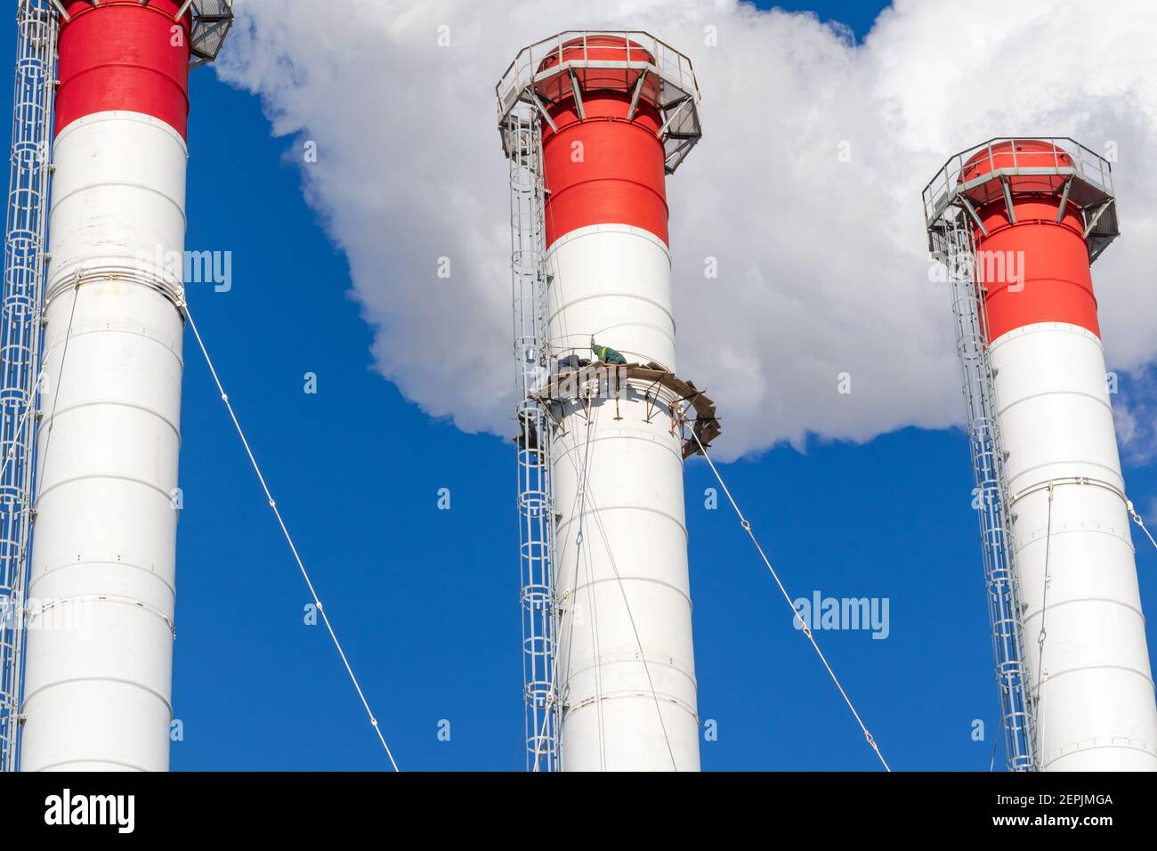 camini rosso-bianco del locale caldaia, dotati di semaforo. scalatori industriali effettuano riparazioni di routine. fumo bianco su un backgro blu cielo Foto Stock