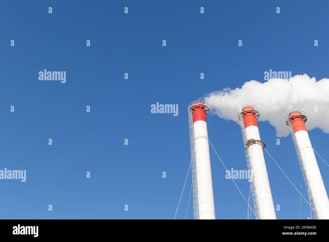 camini rosso-bianco del locale caldaia, dotati di un semaforo. fumo bianco contro il cielo blu nella soleggiata giornata invernale gelida Foto Stock