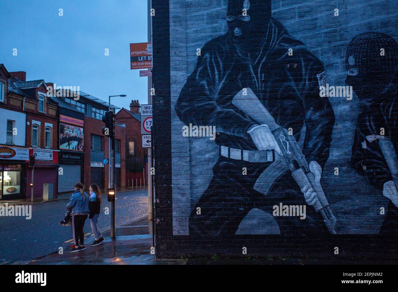 BELFAST, IRLANDA DEL NORD - Febbraio, 23: Due bambini che passano davanti a un murale paramilitare lealista sulla strada di Newtownards il 23 febbraio 2021 . Foto Stock