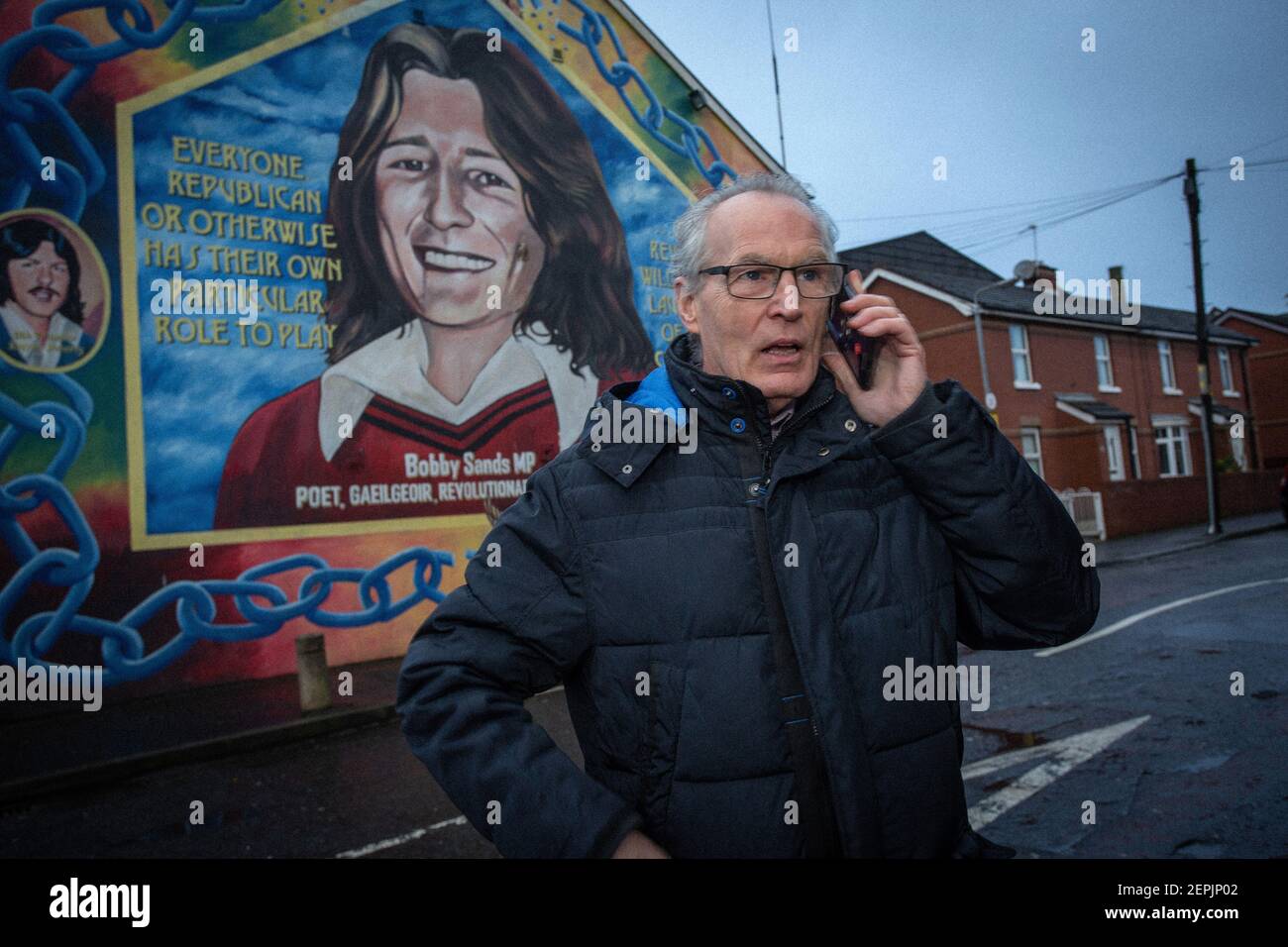 BELFAST, IRLANDA DEL NORD - Febbraio, 23 Gerry Kelly di fronte al murale di Bobby Sands presso la sede centrale del Sinn Fein riceve una chiamata per l'allerta contro la bomba Foto Stock