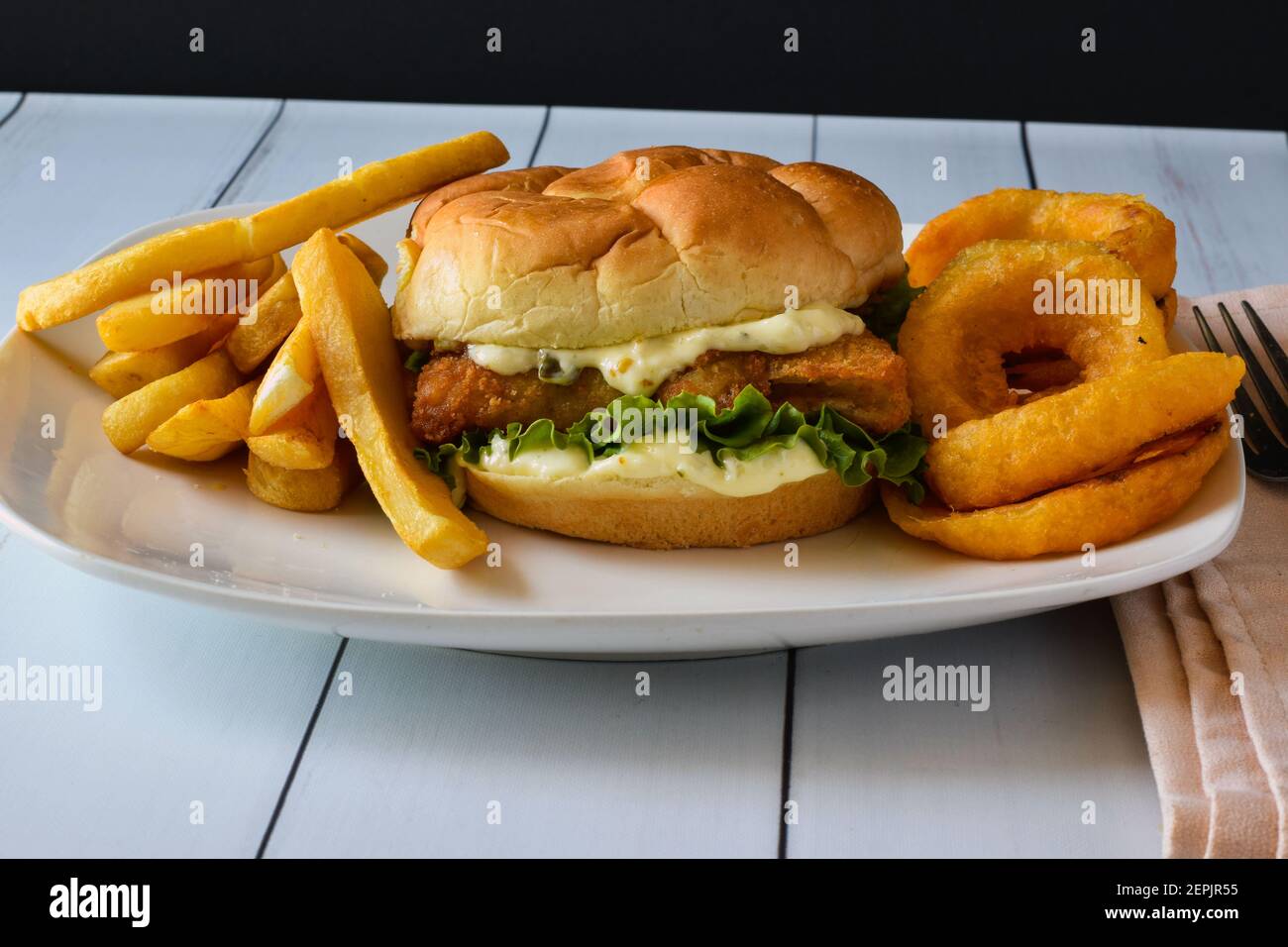 primo piano di sandwich di pesce servito con anelli di cipolla e patatine fritte su un piatto, Foto Stock