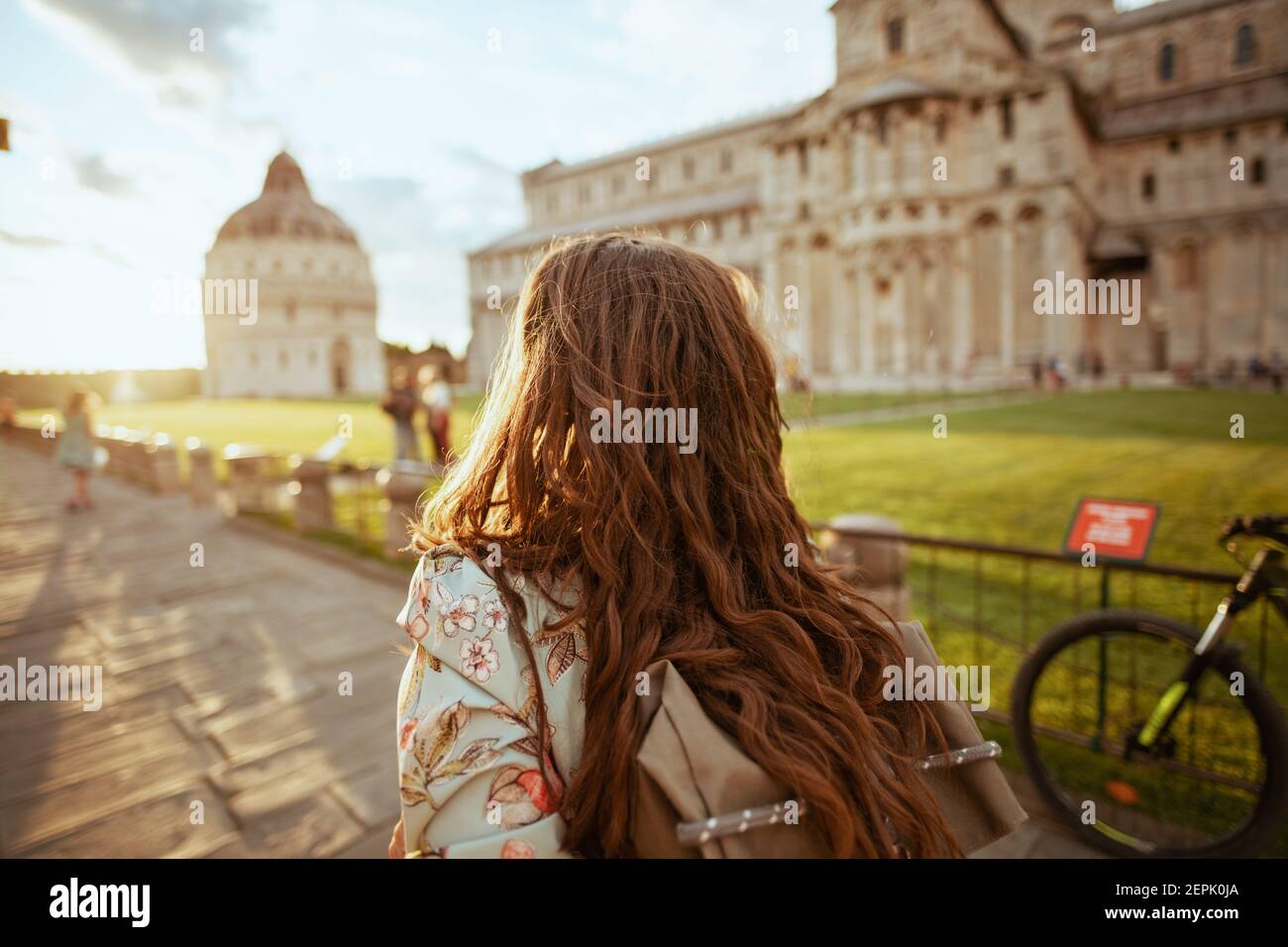 Vista da dietro elegante viaggiatore solista donna in abito floreale con zaino che ha escursione vicino Duomo di Pisa. Foto Stock