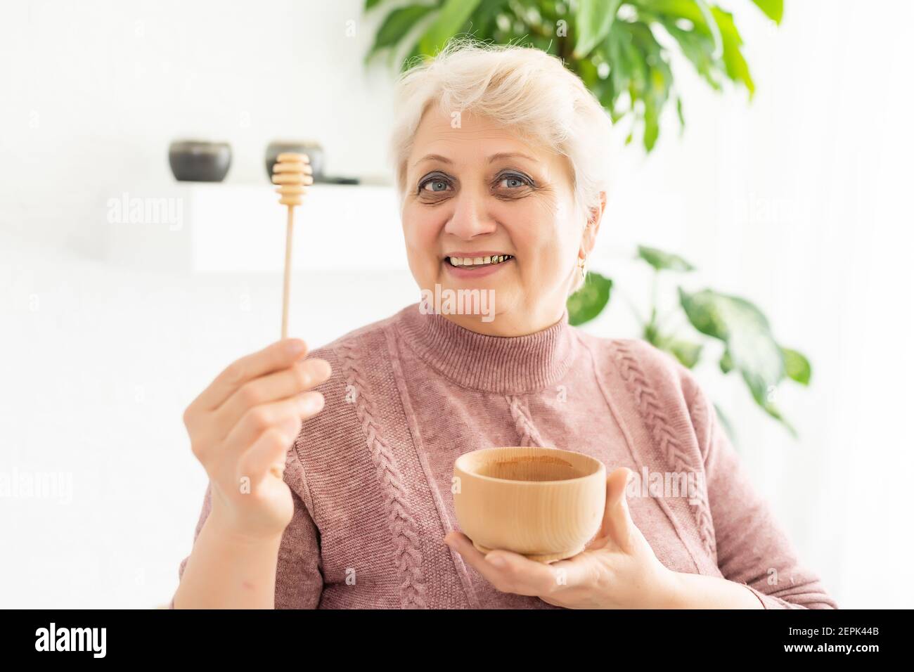 Primo piano ritratto di affascinante donna matura, tenendo il vaso di miele con cucchiaio, guardando la macchina fotografica, isolato su sfondo bianco. Foto Stock