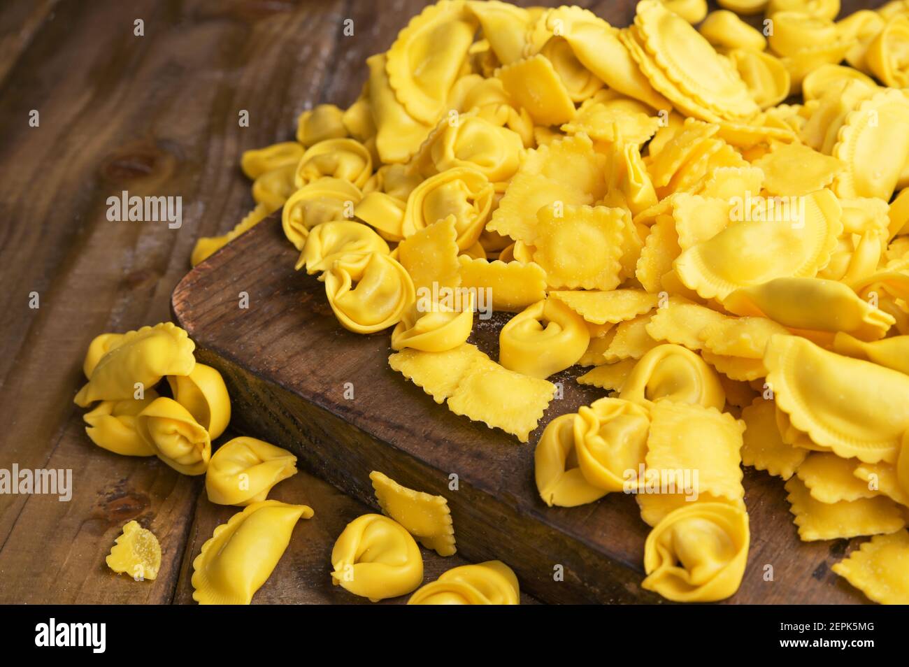 Diversi Tartollini con formaggio o carne per la cottura in brodo, forme diverse. Piatto tradizionale per celebrazioni in italia, regione Emilia Romagna. Pasta fresca fatta in casa con ripieno su un tavolo di legno Foto Stock